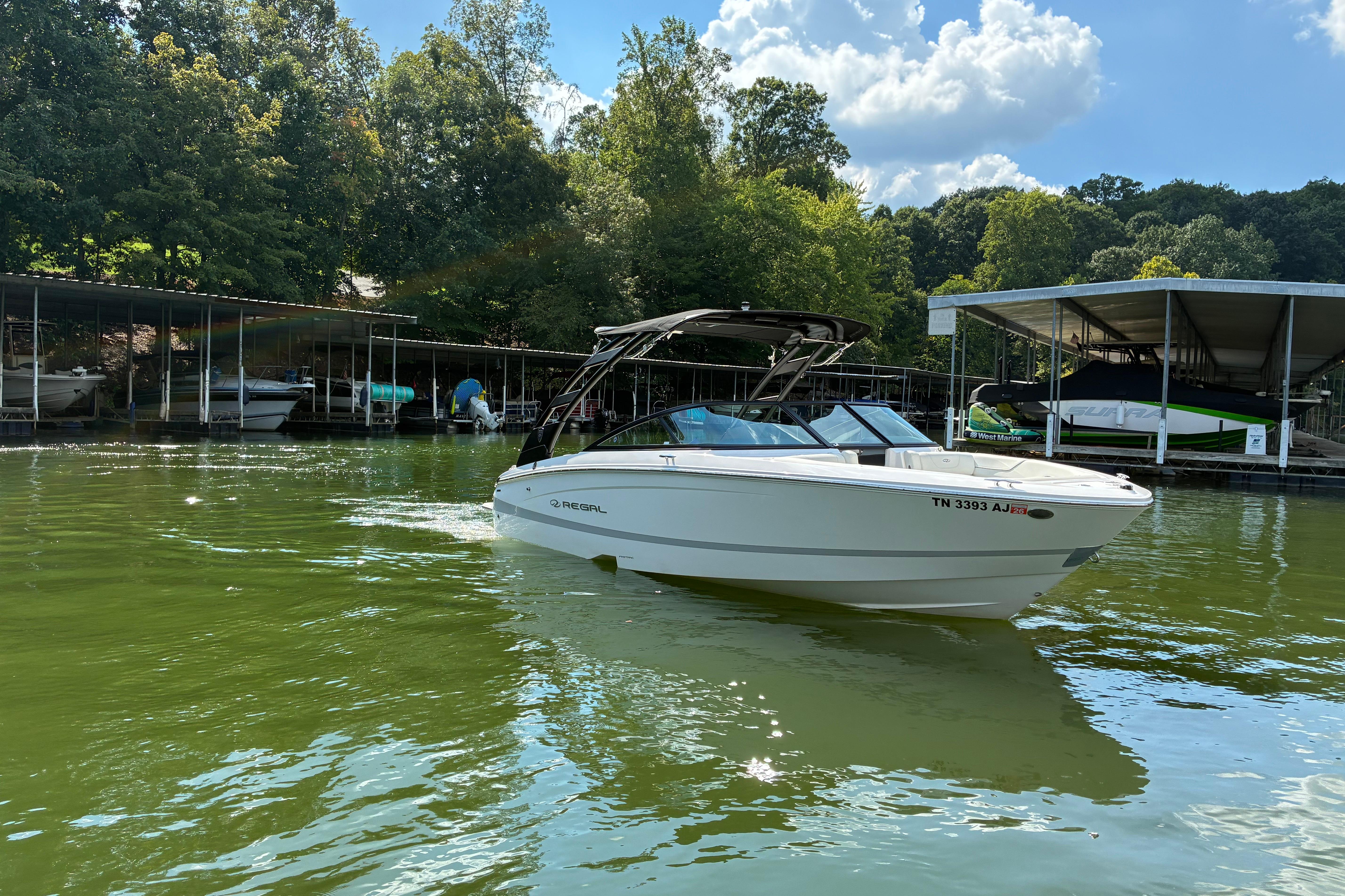 2025 Regal LS2 boat on a serene lake near a marina, surrounded by lush trees.