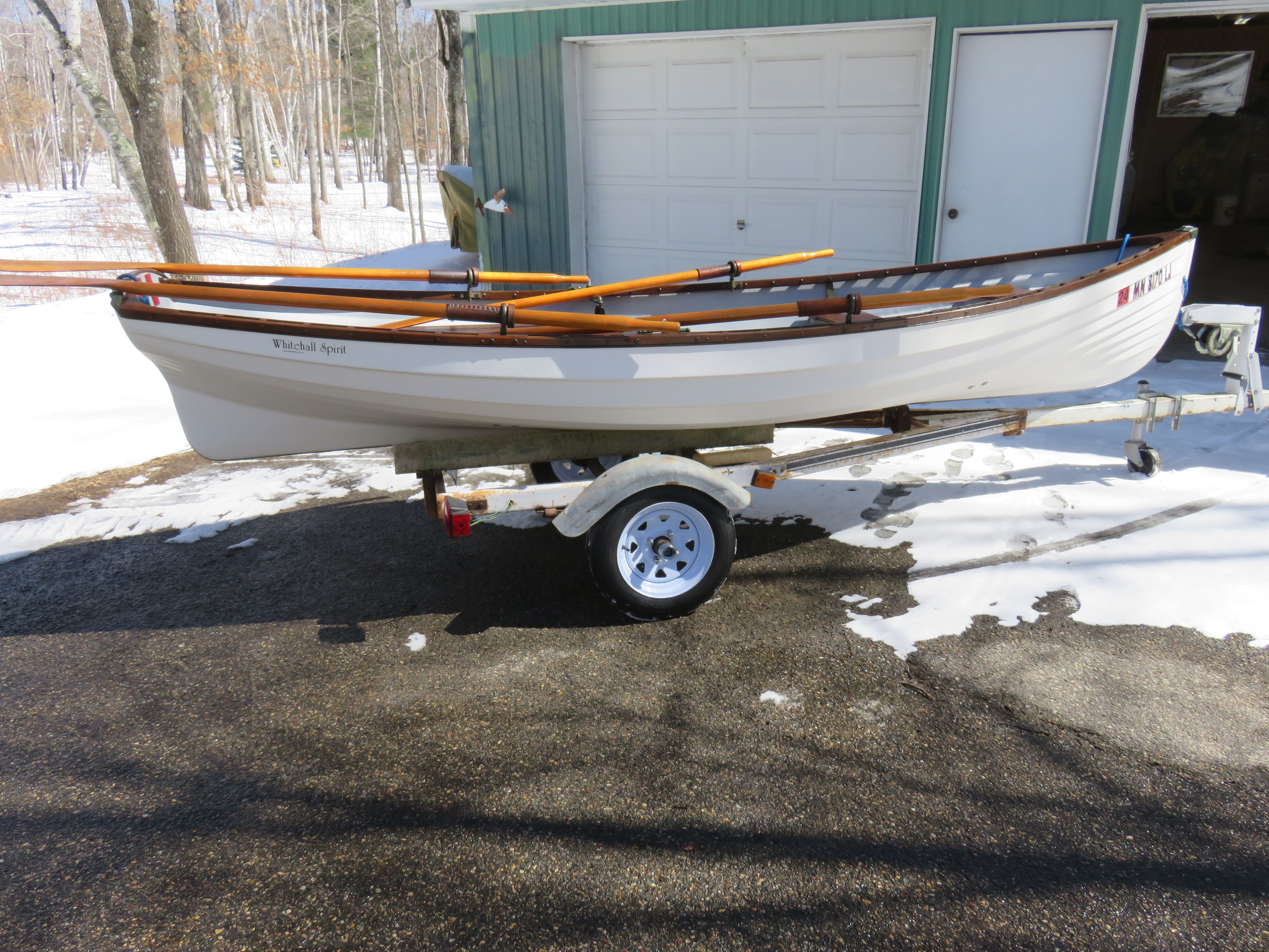 A white rowboat on a trailer outside a garage in a snowy setting.