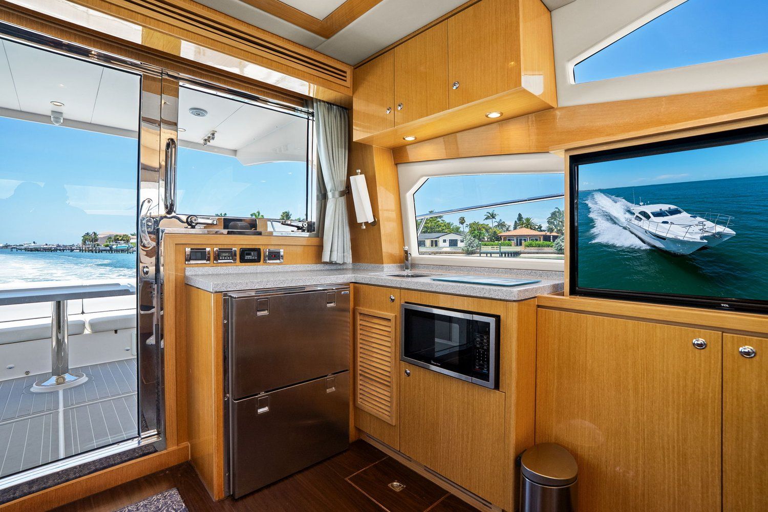 Interior of a modern yacht kitchen with wooden cabinets, microwave, and sea view.
