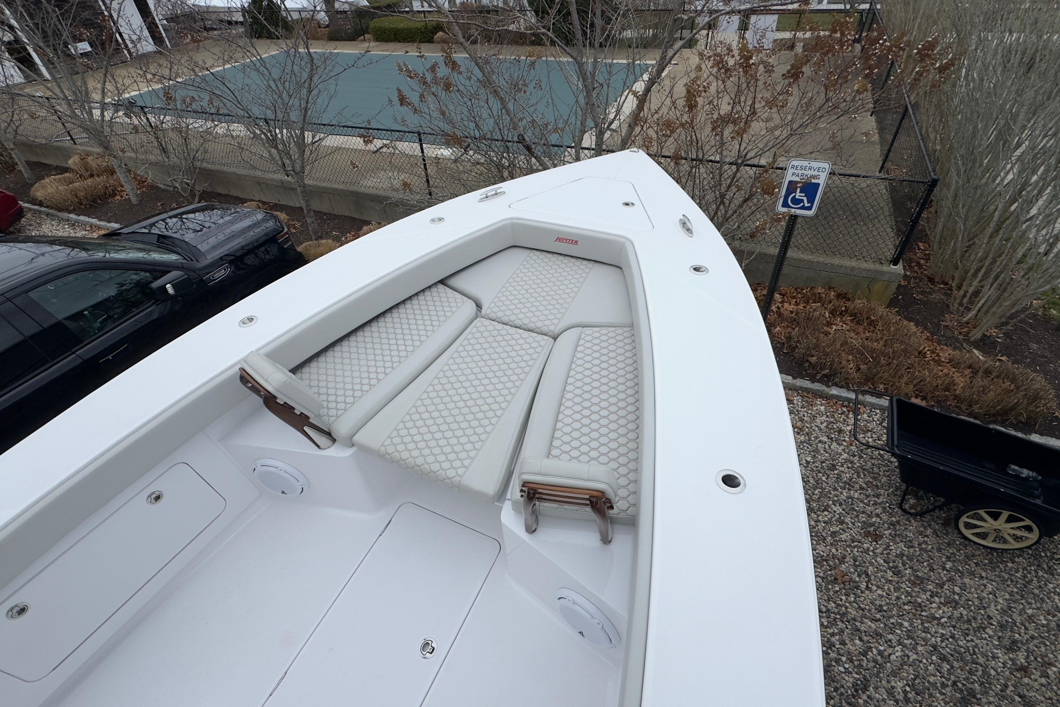 2024 Jupiter 32 FS boat with cushioned seating, parked near a pool and reserved parking sign.
