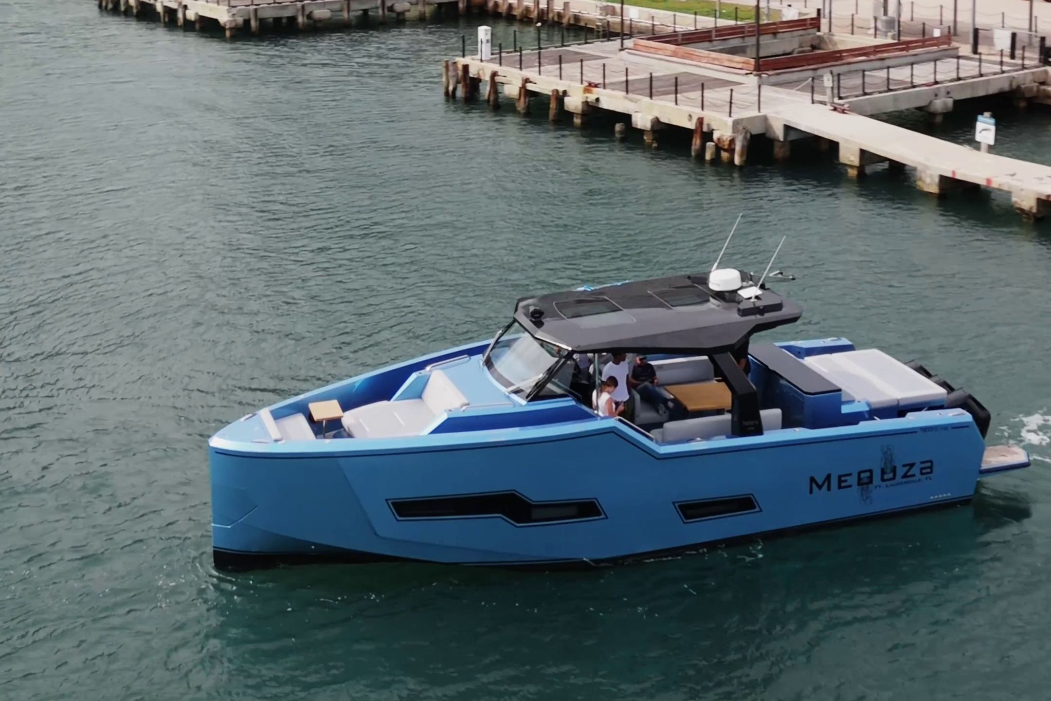 A modern blue motorboat cruising in a harbor. It features an open deck and luxurious seating.