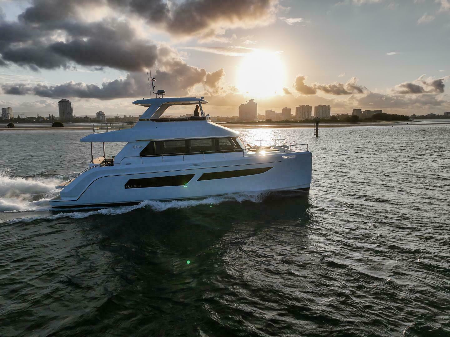 Luxury yacht ILIAD 53F cruising at sunset, 2026 model, with city skyline in background.