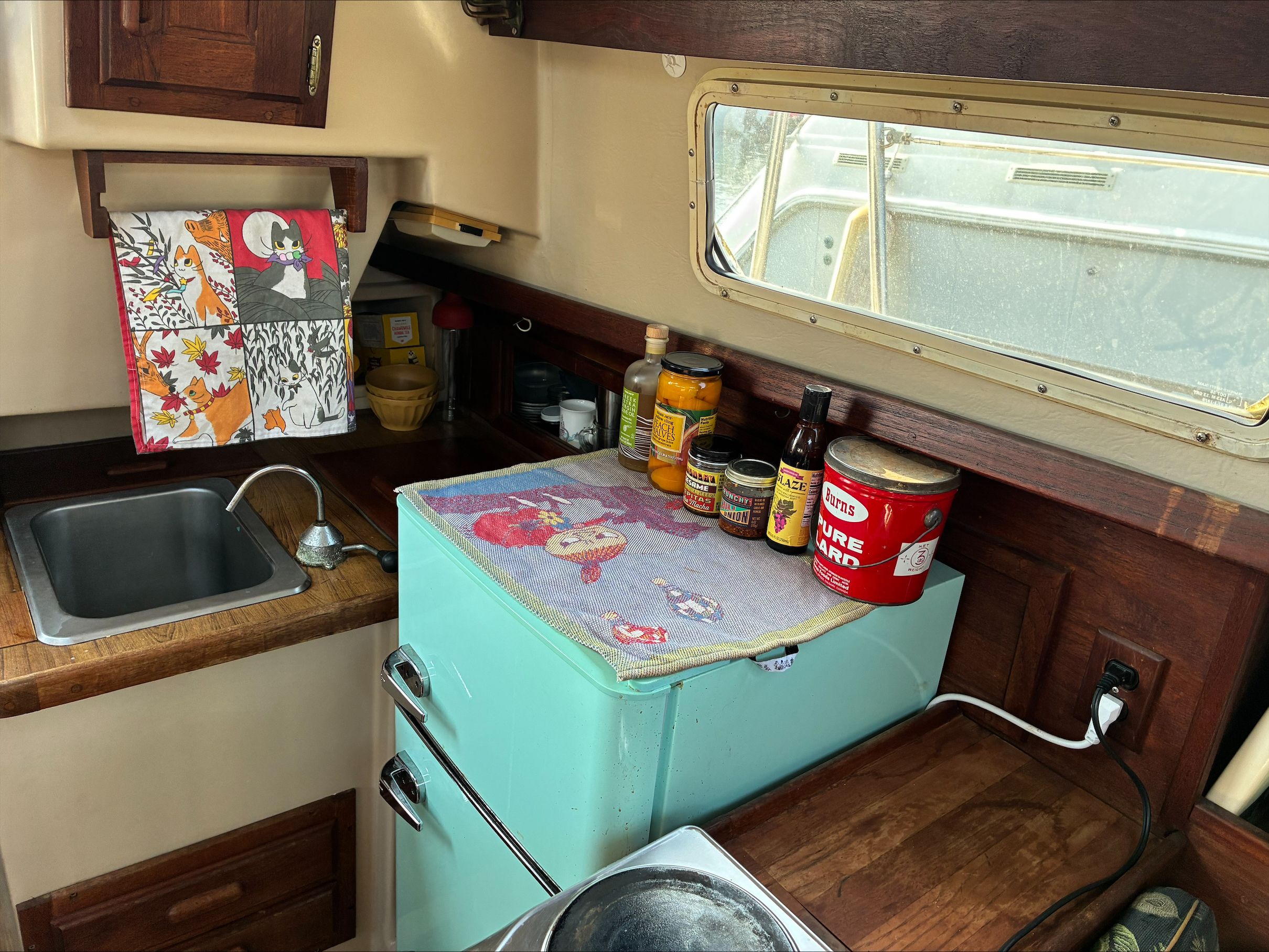 Small boat kitchen with sink, fridge, and spices on the counter.