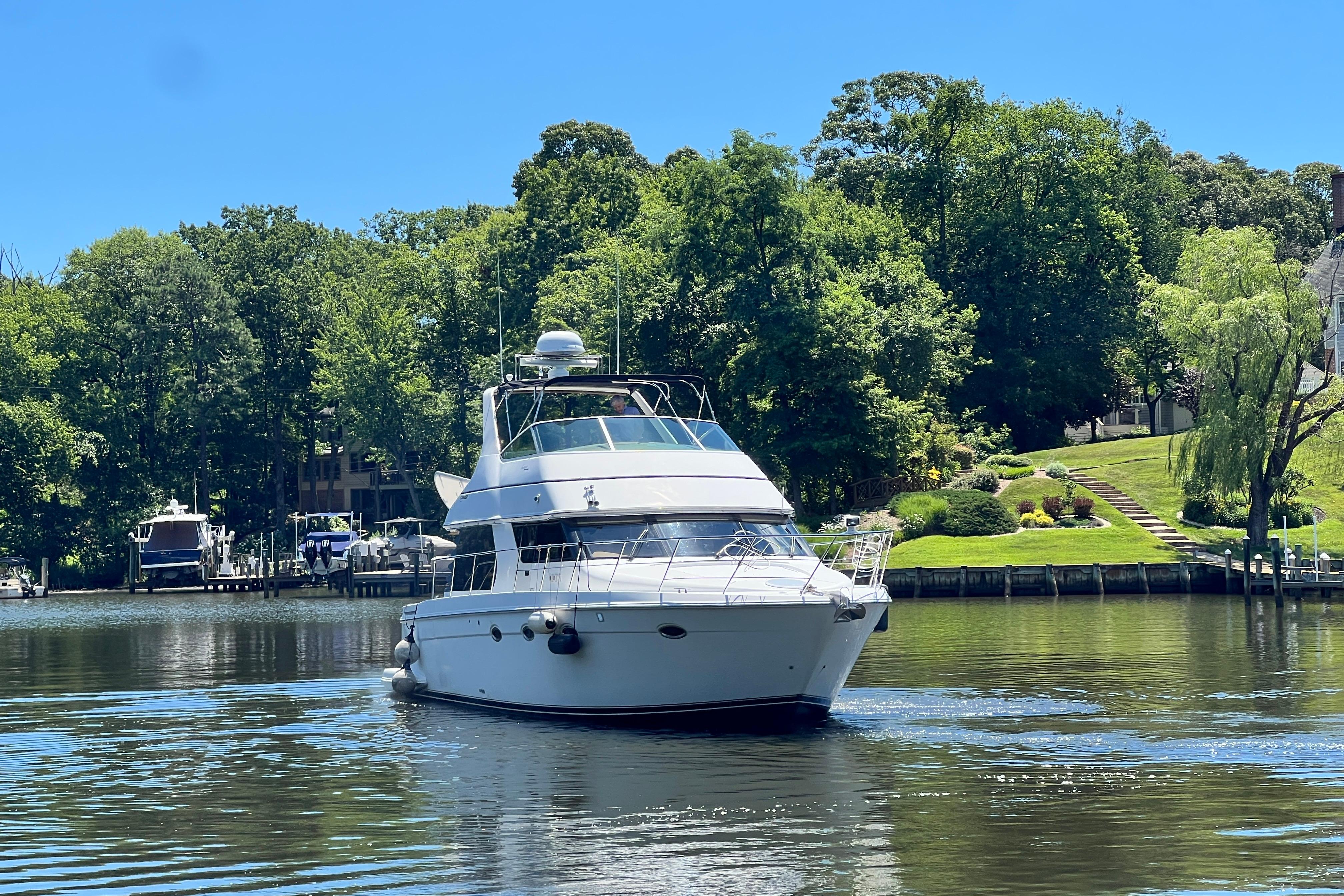 2003 Carver 450 Voyager Pilothouse yacht on a serene river, surrounded by lush greenery.