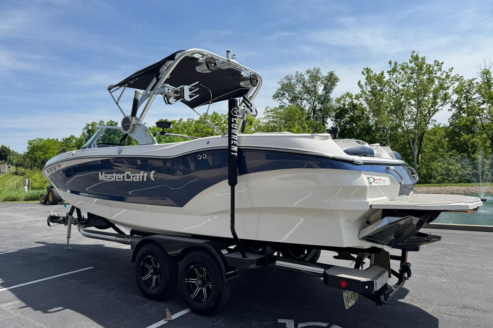 2021 MasterCraft X24 boat on trailer, parked outdoors with trees in background.