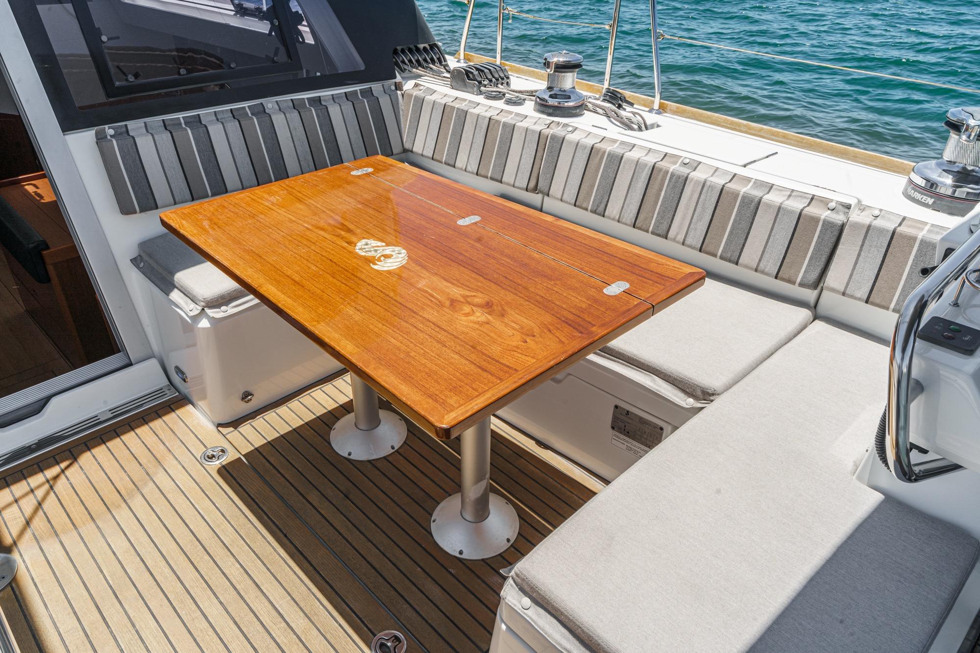 Cockpit seating area on a 2017 Beneteau Sense 50 yacht with wooden table and striped cushions.