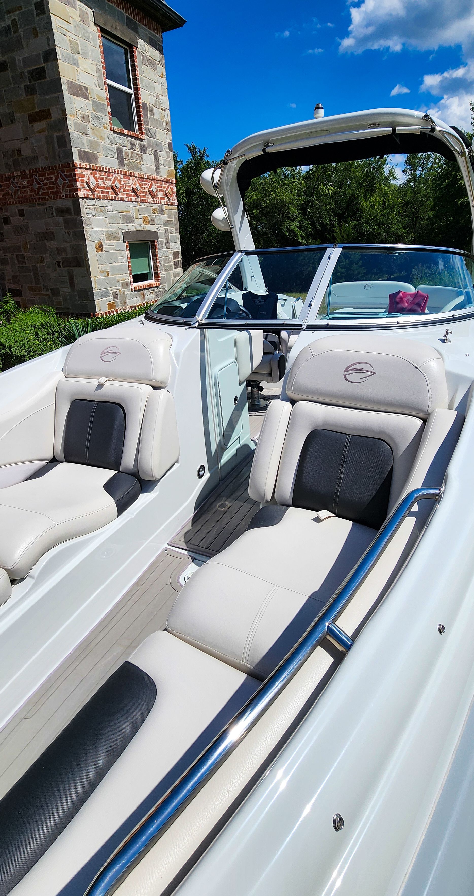 A 2017 Crownline 285SS boat with white and black seats, near a stone house.
