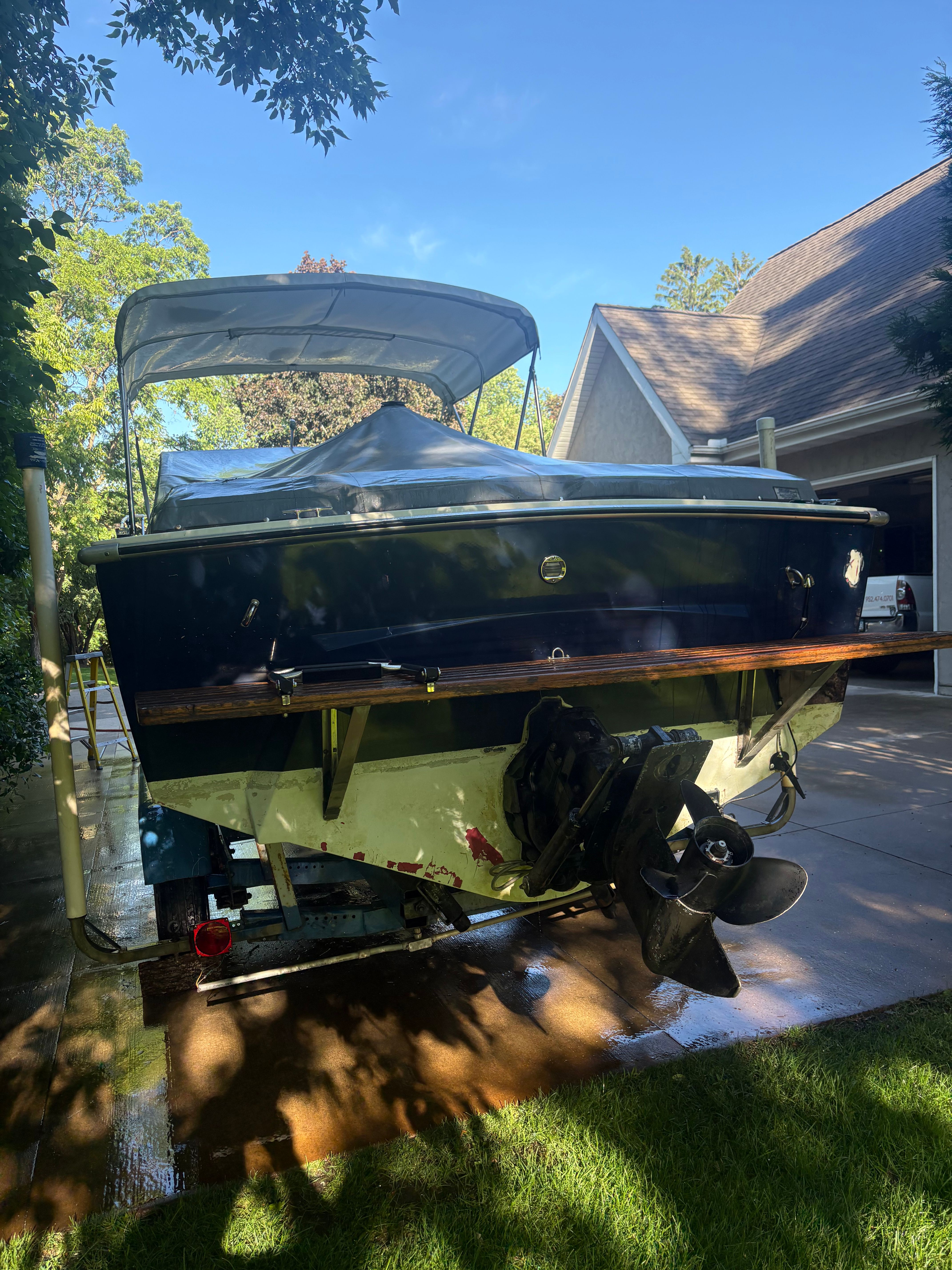 A 1976 Formula 233 boat on a driveway. It has a blue stern and a canopy.