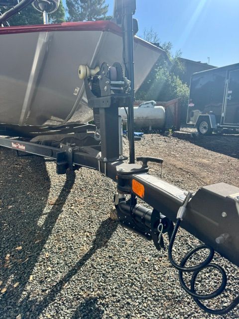 A Bass Tracker boat on a trailer, surrounded by gravel and a trailer in the background.