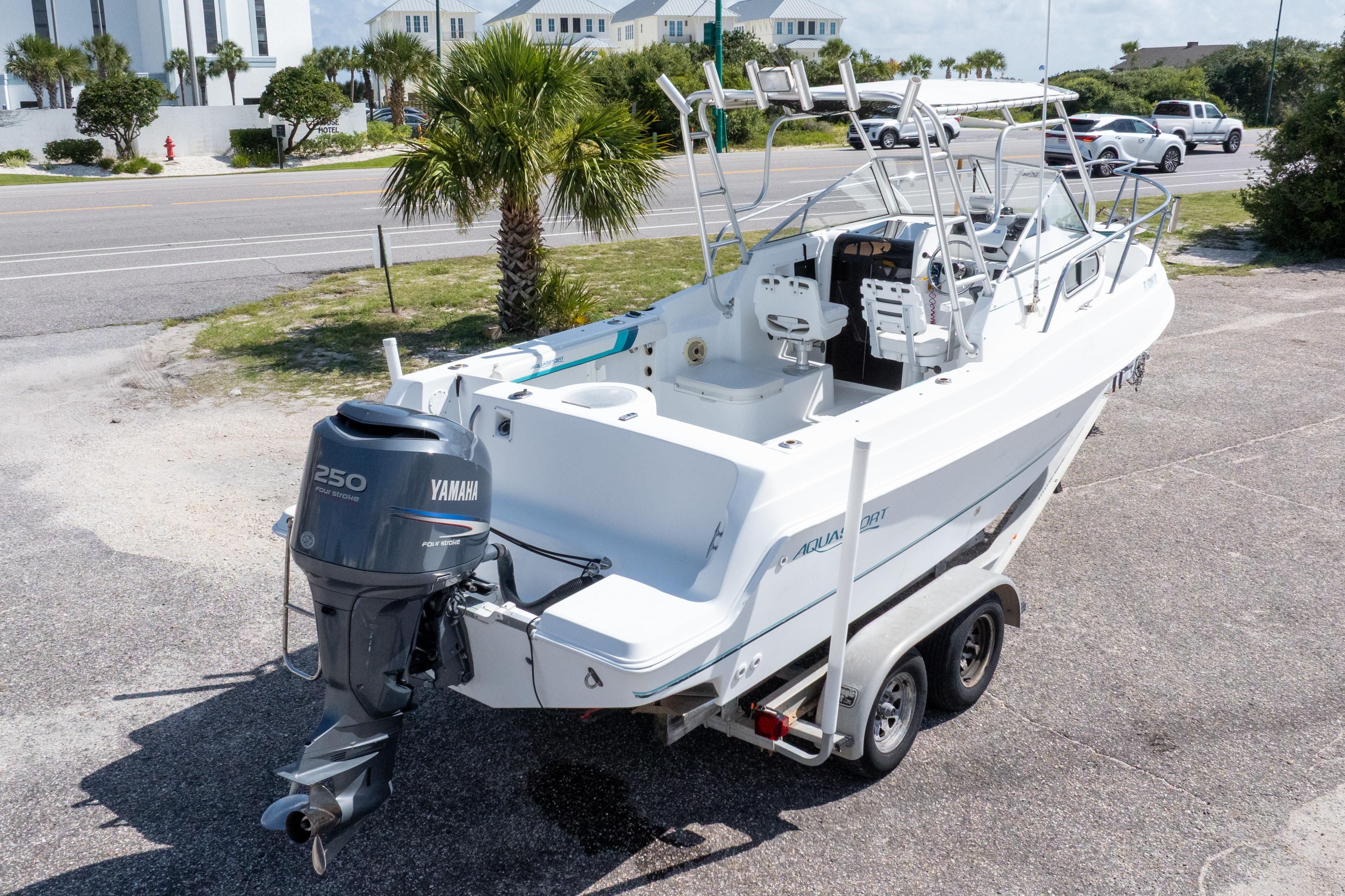 1999 Aquasport 225 Explorer boat with Yamaha 250 engine on a trailer, parked near palm trees.