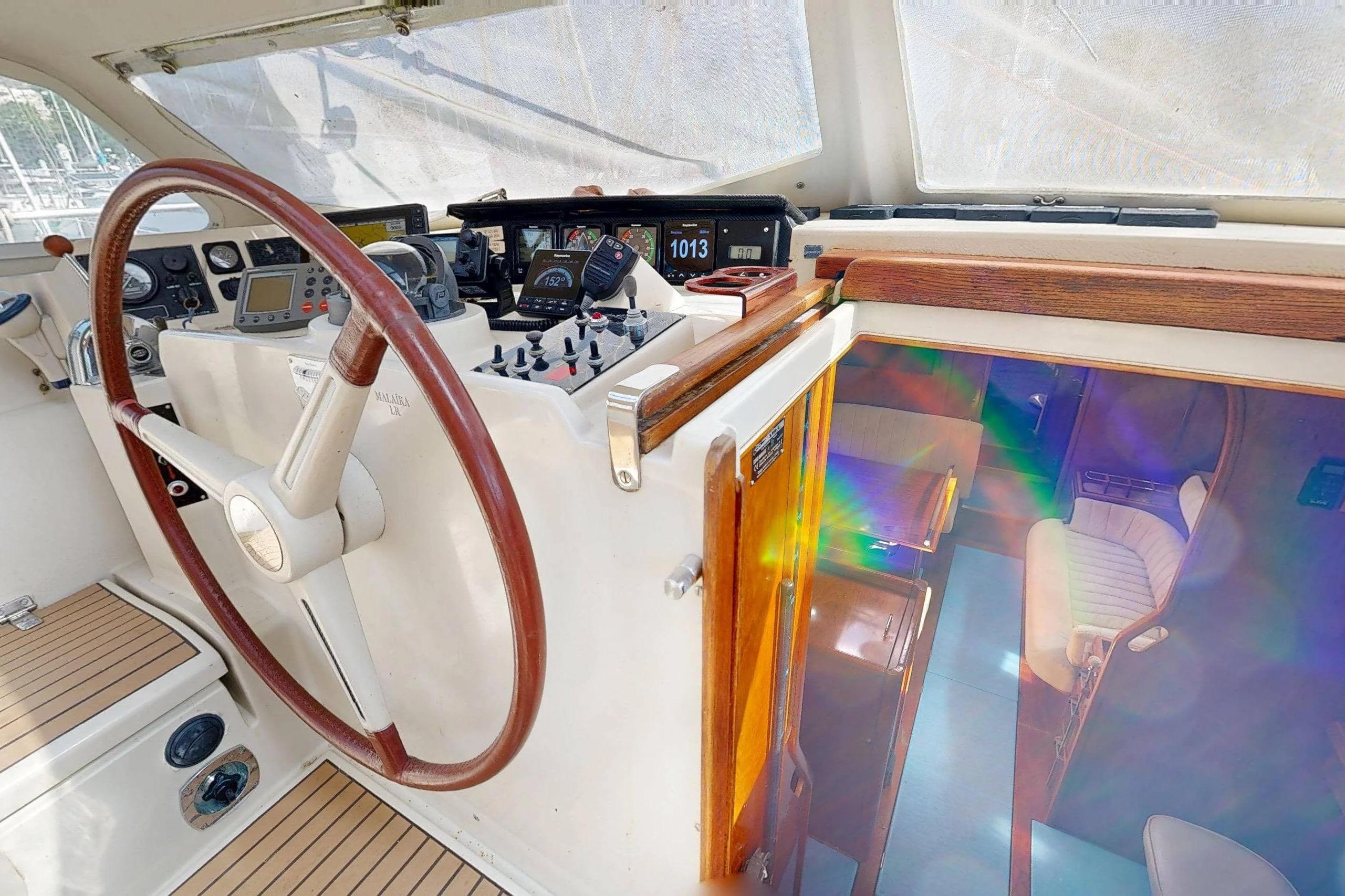 Cockpit of 1999 Amel Super Maramu 2000 sailboat with wooden steering wheel and navigation instruments.