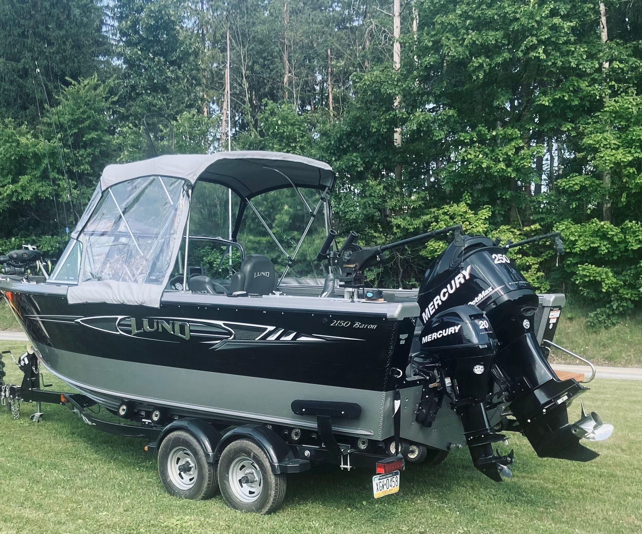 A 2012 Lund Baron boat on a trailer, set on grass with trees in the background.
