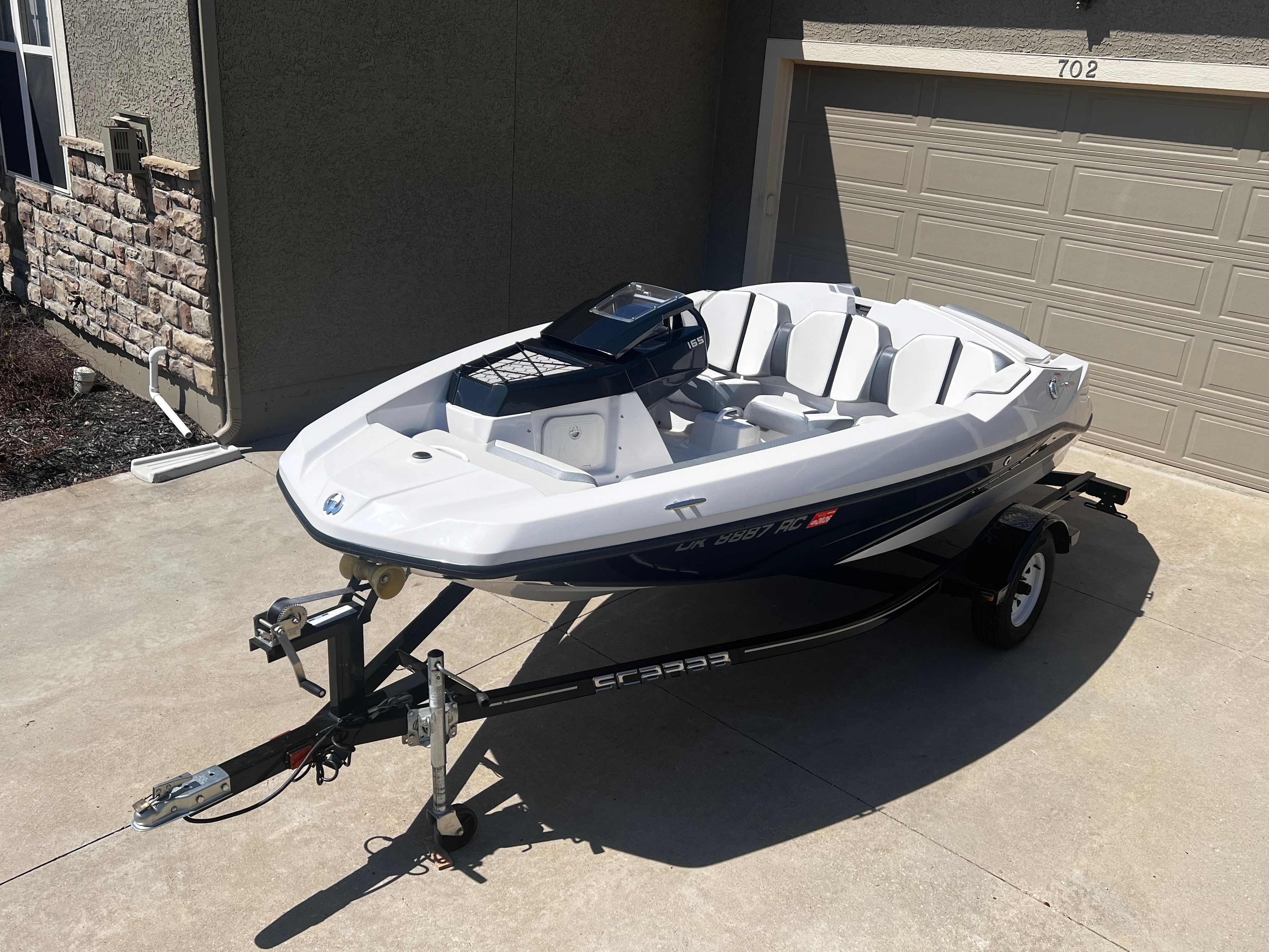 A white 2019 Scarab 165 G boat on a trailer in a driveway.