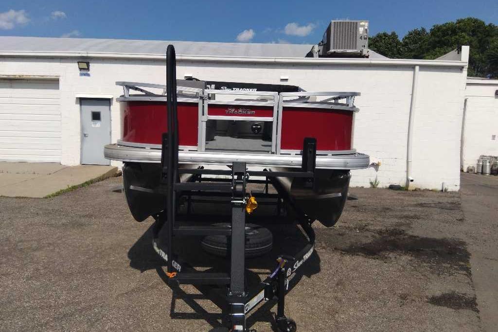 2026 Sun Tracker Bass Buggy 18 DLX pontoon boat on trailer, parked outside a building.