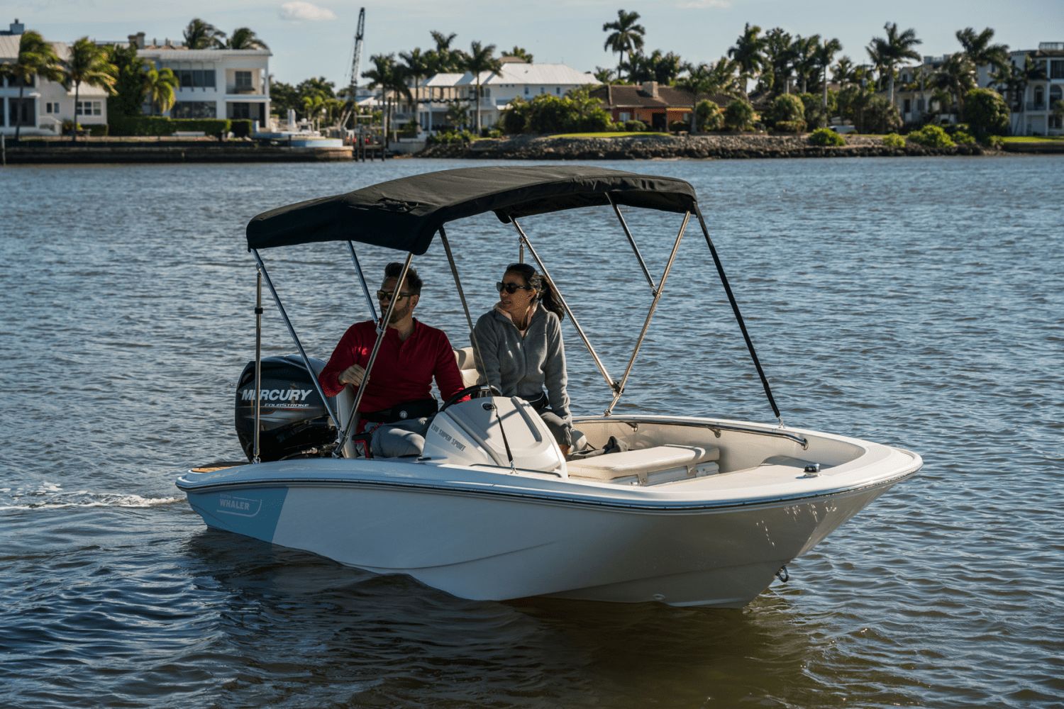 Two people ride a Boston Whaler 130 Super Sport on calm waters.