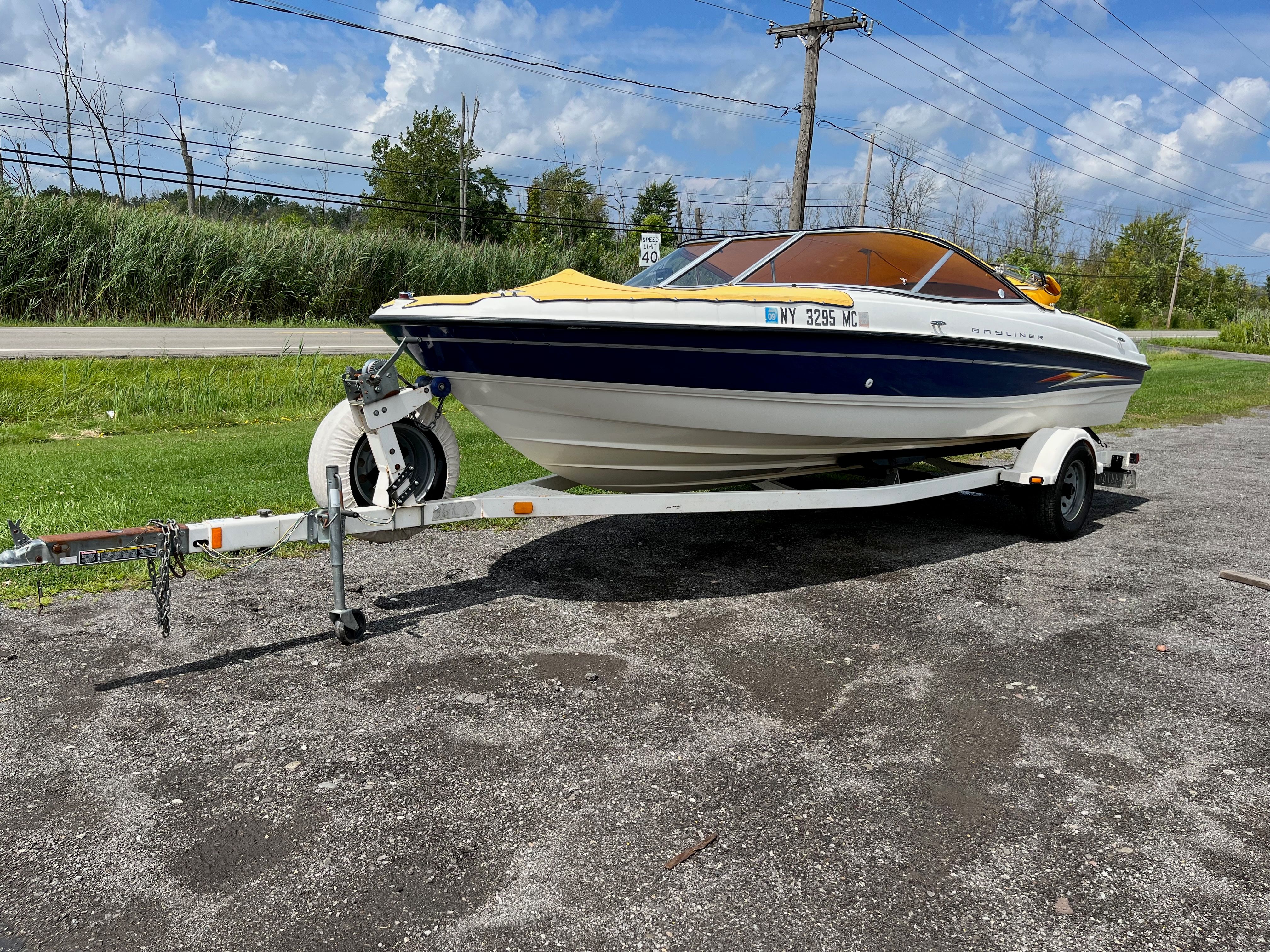 A 2005 Bayliner 205BR on a trailer, parked on a gravel lot beside a road.