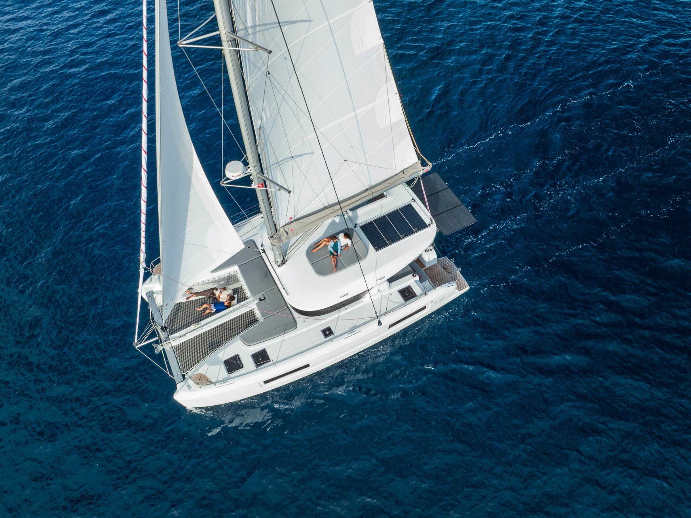 Aerial view of 2025 Lagoon 38 catamaran sailing on clear blue ocean waters.