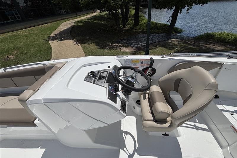 2026 Tahoe 2150 boat cockpit with steering wheel and seating, near a lakeside path.