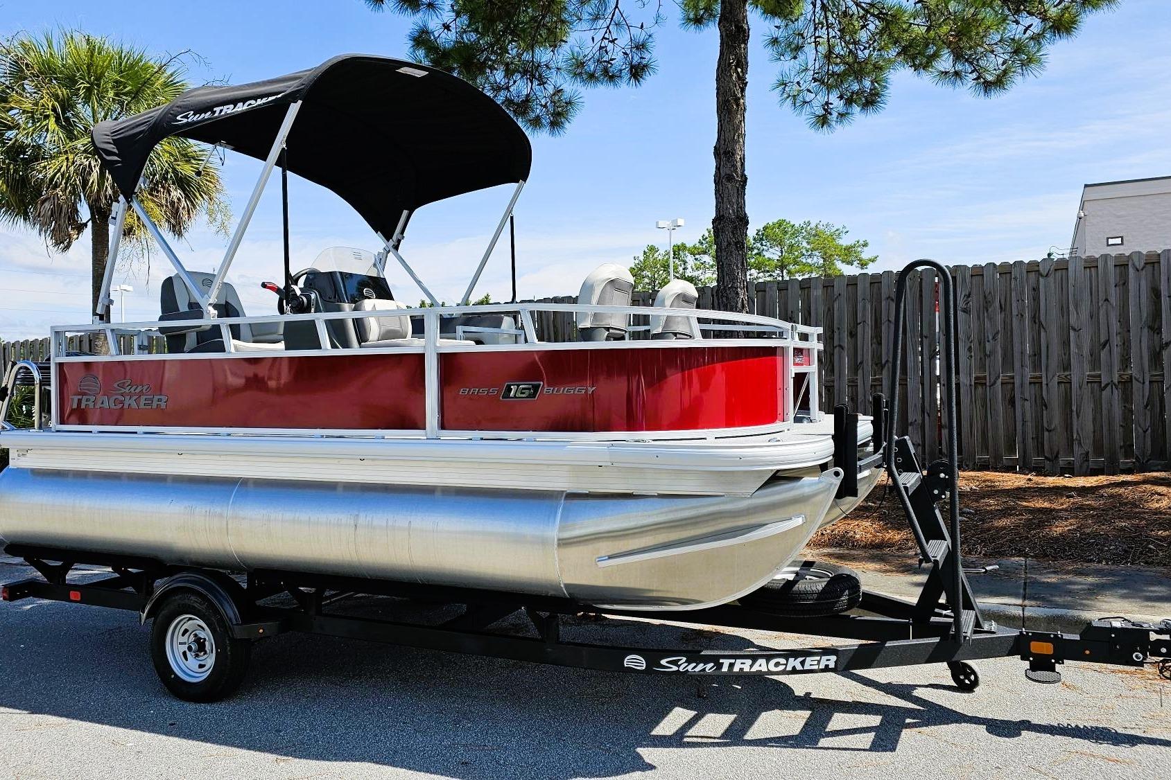 2026 Sun Tracker Bass Buggy 16 XL Select pontoon boat on trailer, parked outdoors.