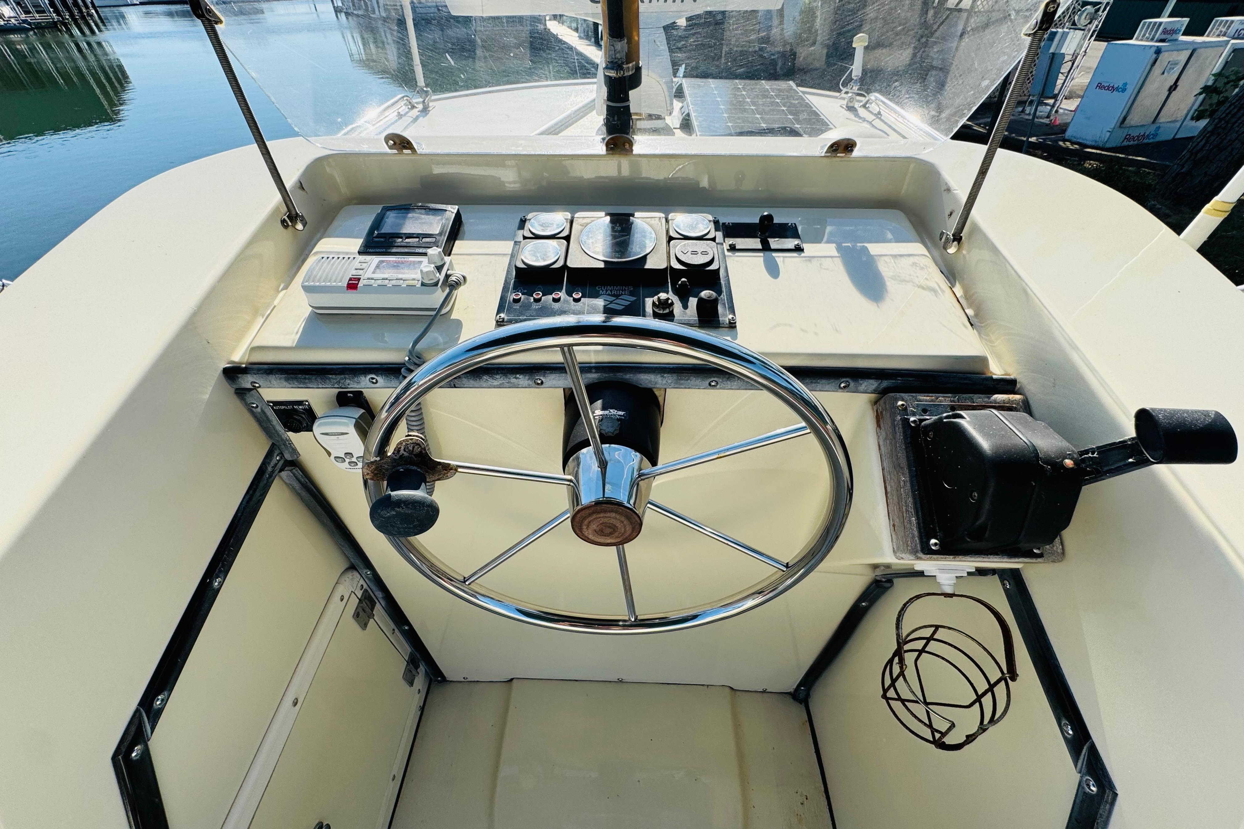 1996 Nordic Tug 32 helm with steering wheel and control panel, docked by the water.