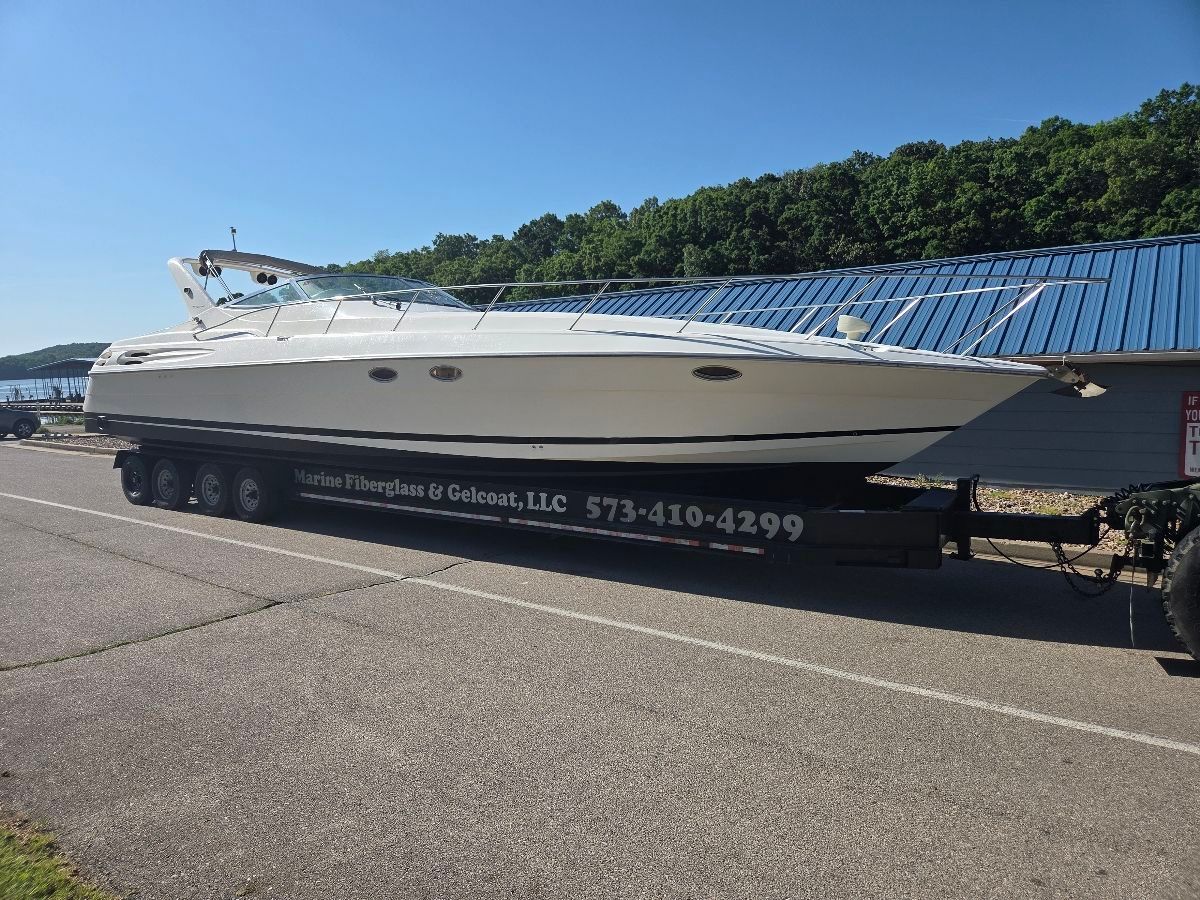 A white boat on a trailer is parked on a road next to a blue building.