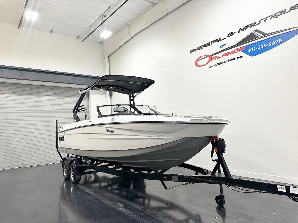 2025 Supreme S240 boat on trailer in showroom, white hull, black canopy.