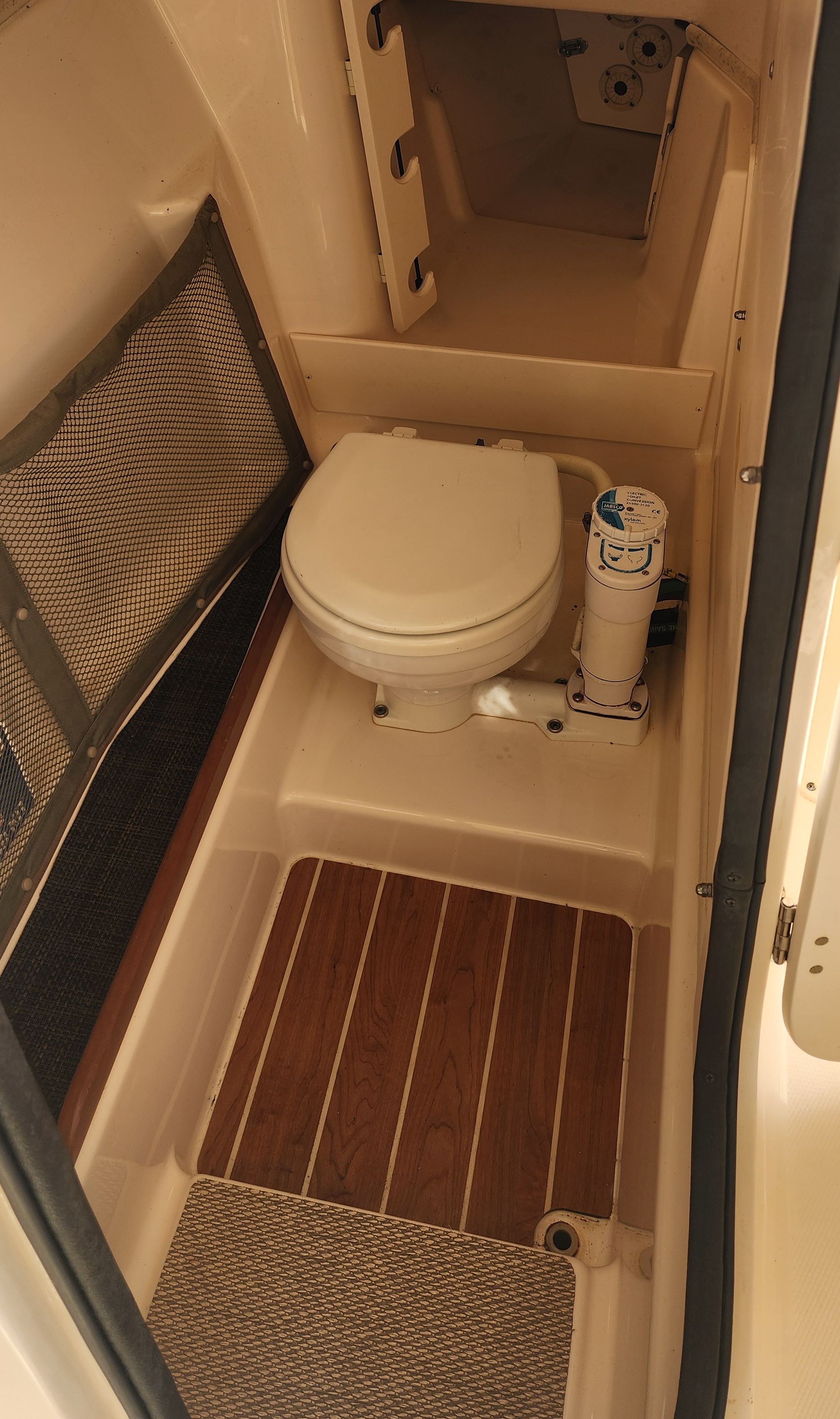 The image shows a boat toilet with a wooden floor and mesh storage.