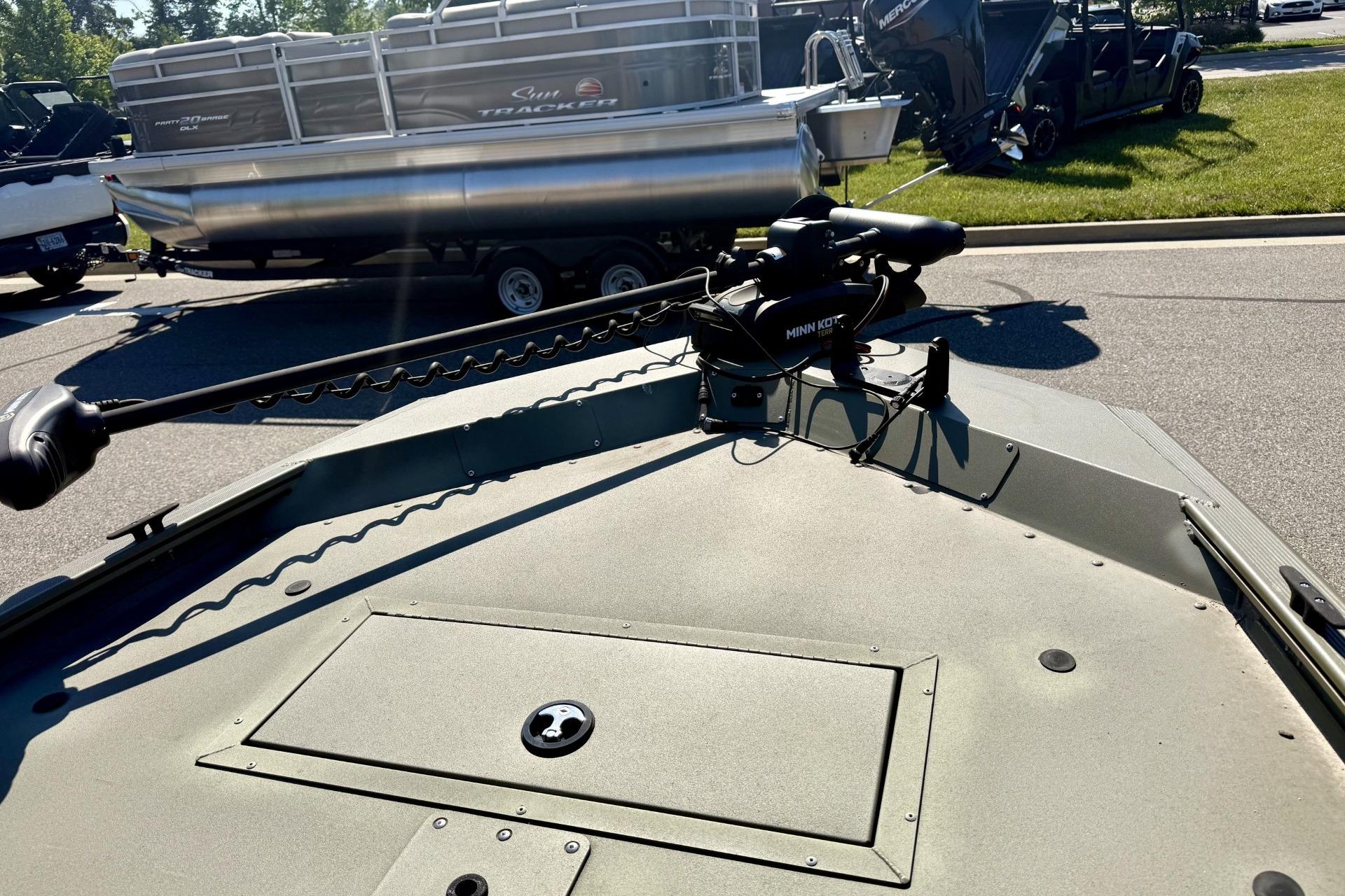 2024 Tracker Grizzly 1648 Jon boat with Minn Kota trolling motor, parked near a pontoon.
