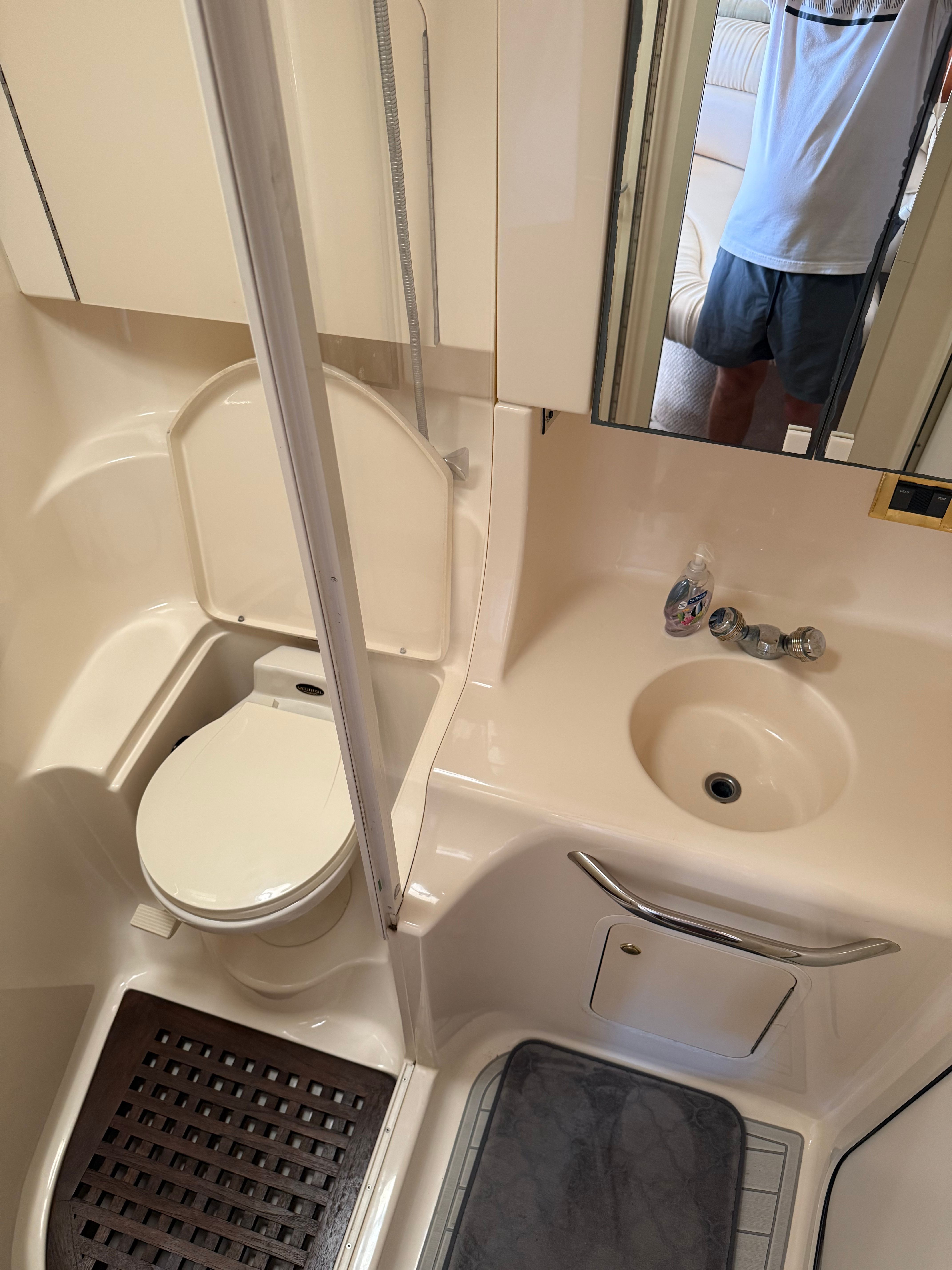 The bathroom of a yacht with a toilet, sink, and mirror.