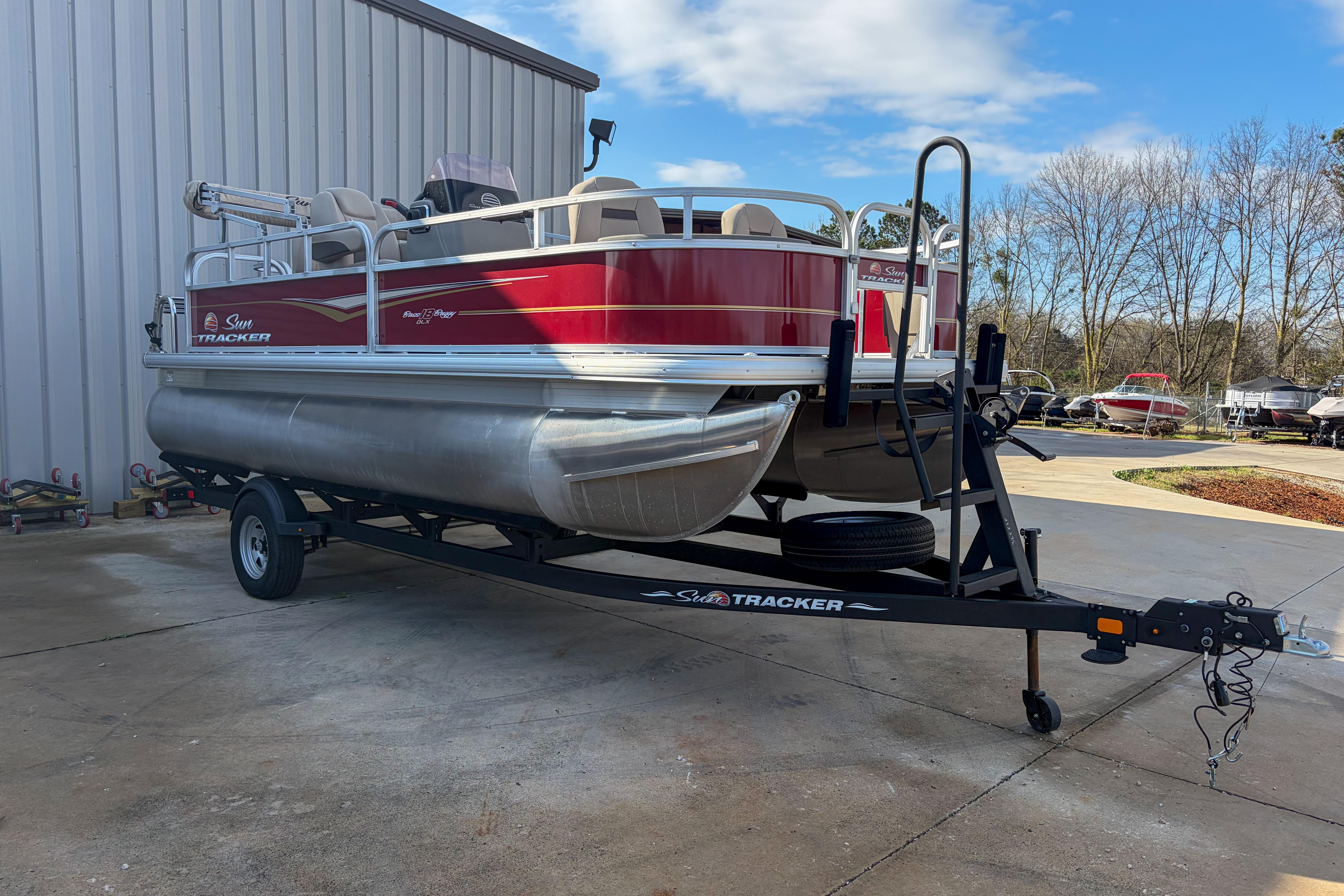 2024 Sun Tracker Bass Buggy 18 DLX pontoon boat on trailer, parked outdoors.