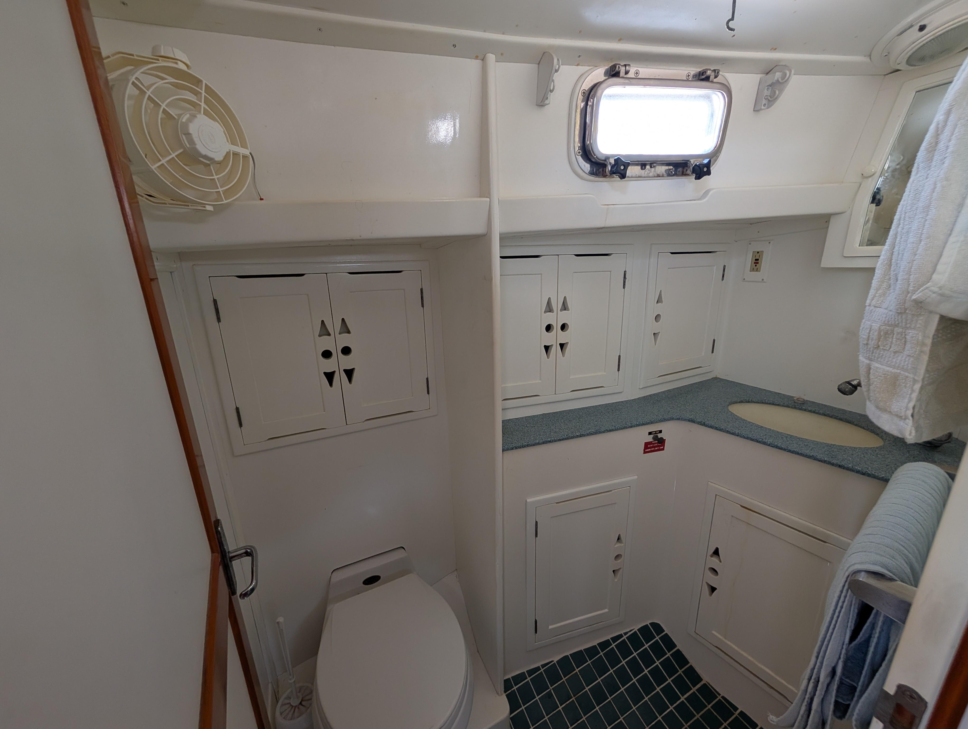 1996 Cabo Rico Northeast 400 yacht bathroom with white cabinets, toilet, and small window.