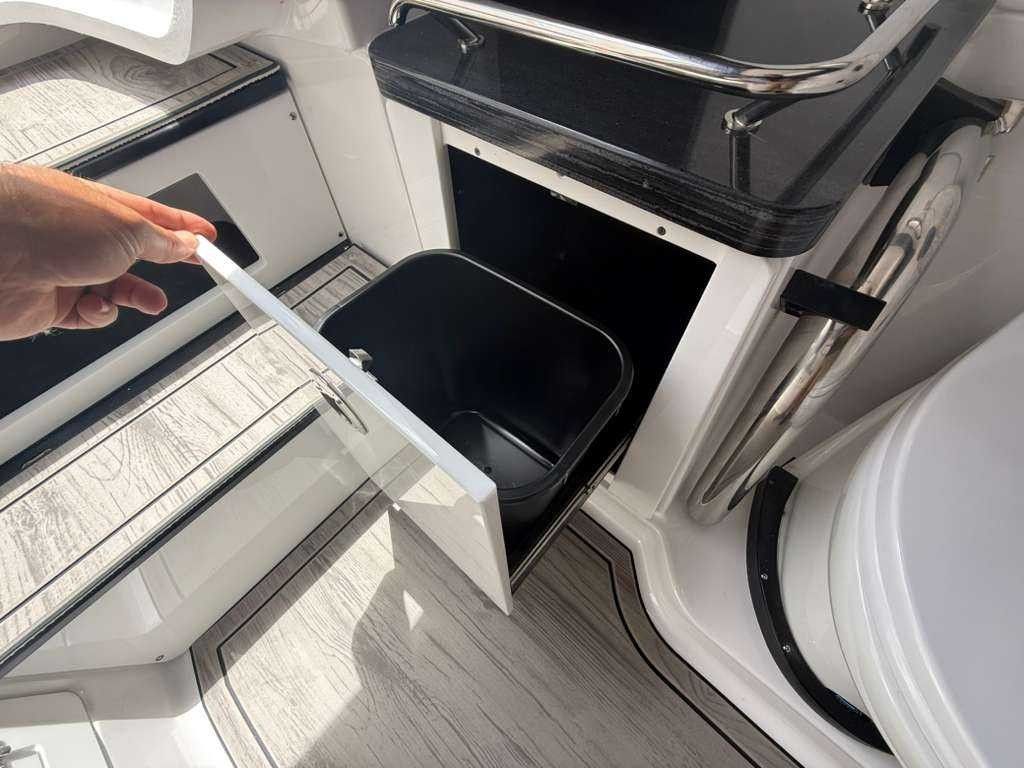 A trash bin inside a boat cabinet with an open door.