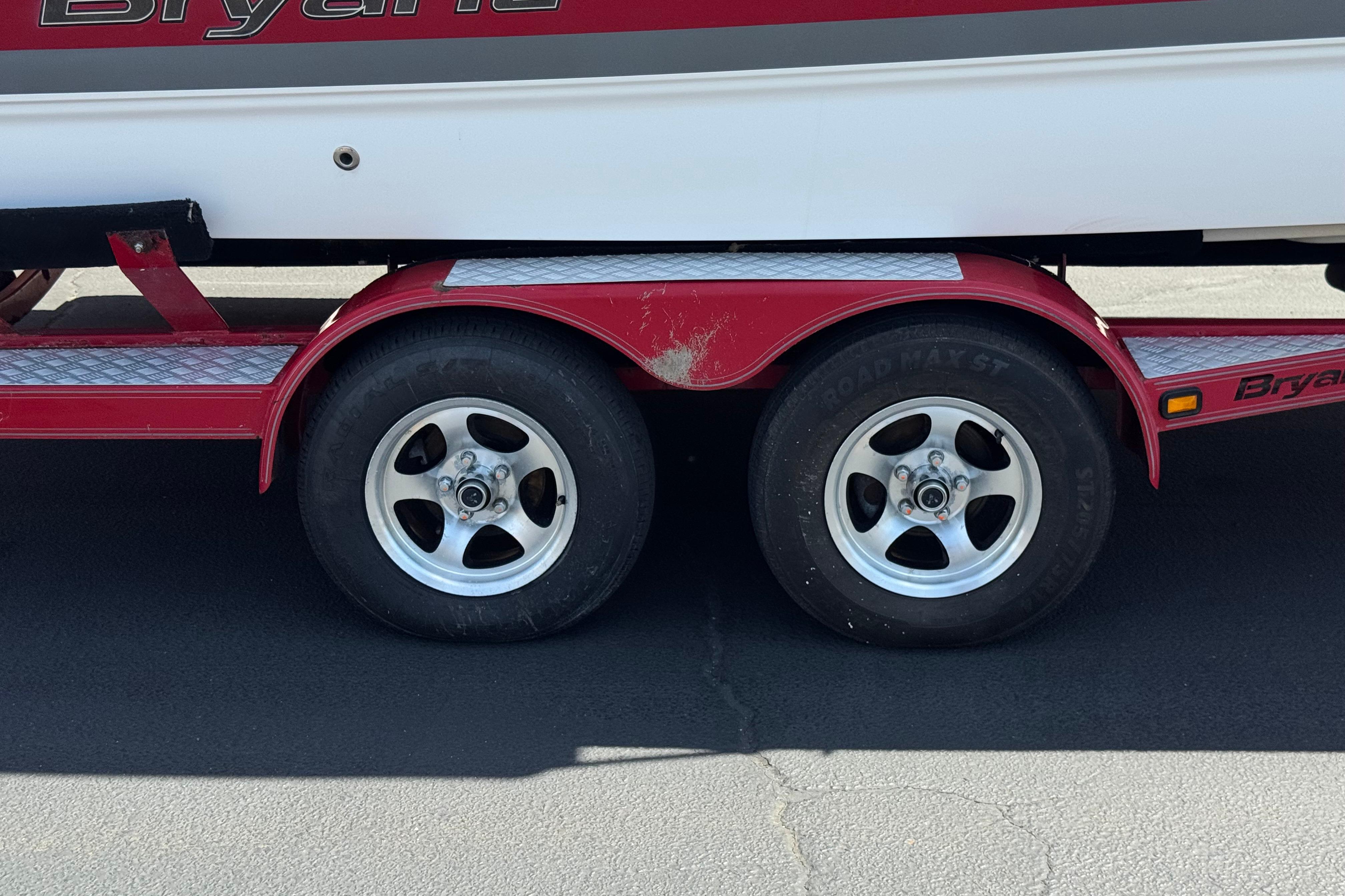 Red trailer with dual wheels for a 2010 Bryant 255 boat on asphalt.