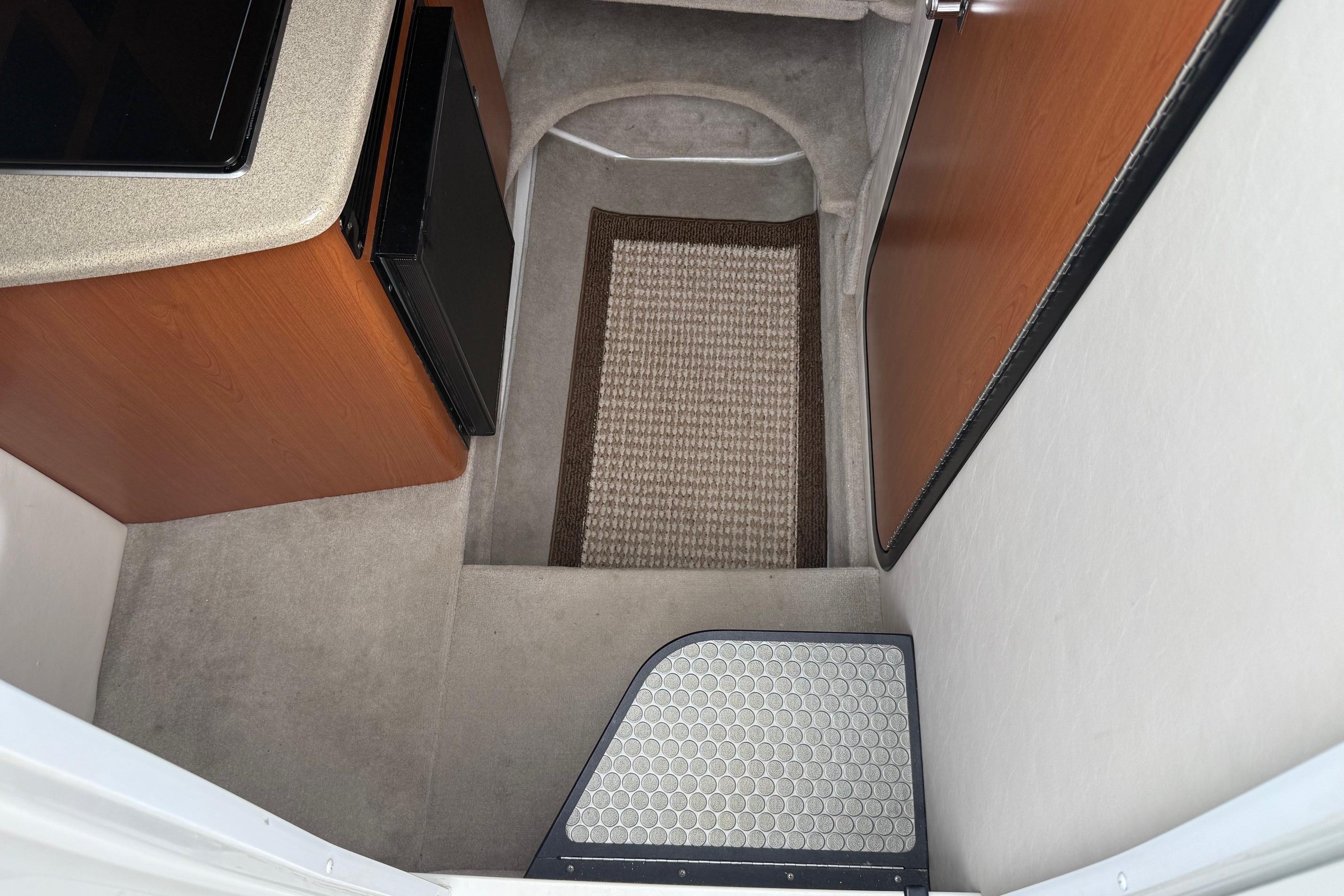 Interior view of a 2005 Crownline 250 CR boat cabin with carpet and compact kitchenette.