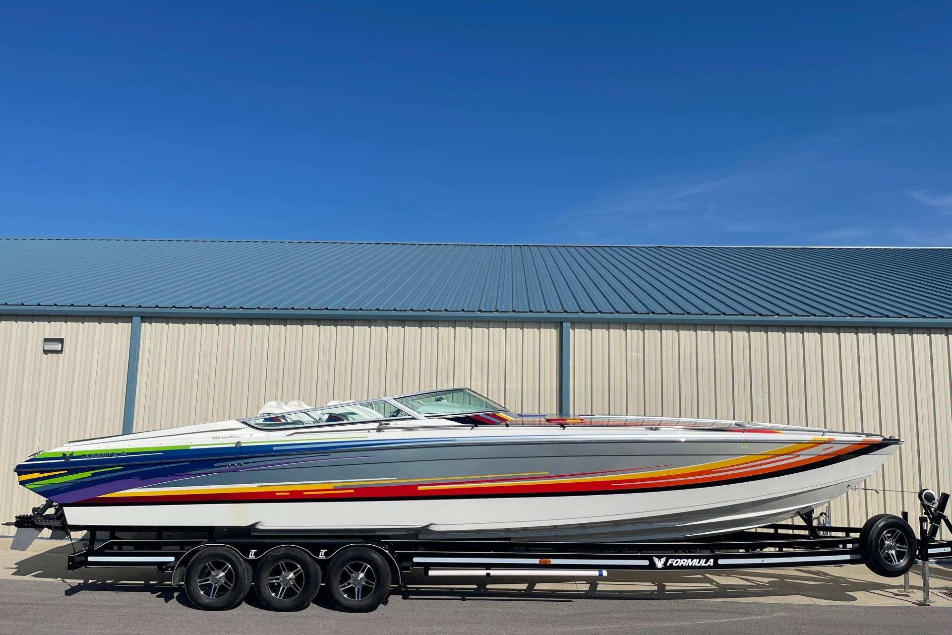 2004 Formula 382 FASTech boat on trailer, vibrant design, parked by metal building.