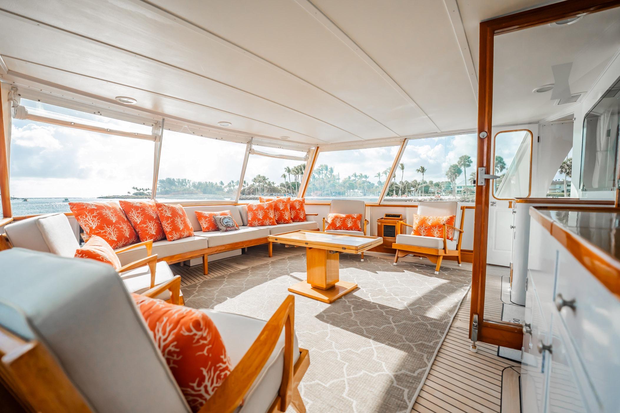 Luxurious 1972 Trumpy 72 Motor Yacht interior with vibrant orange cushions and panoramic windows.