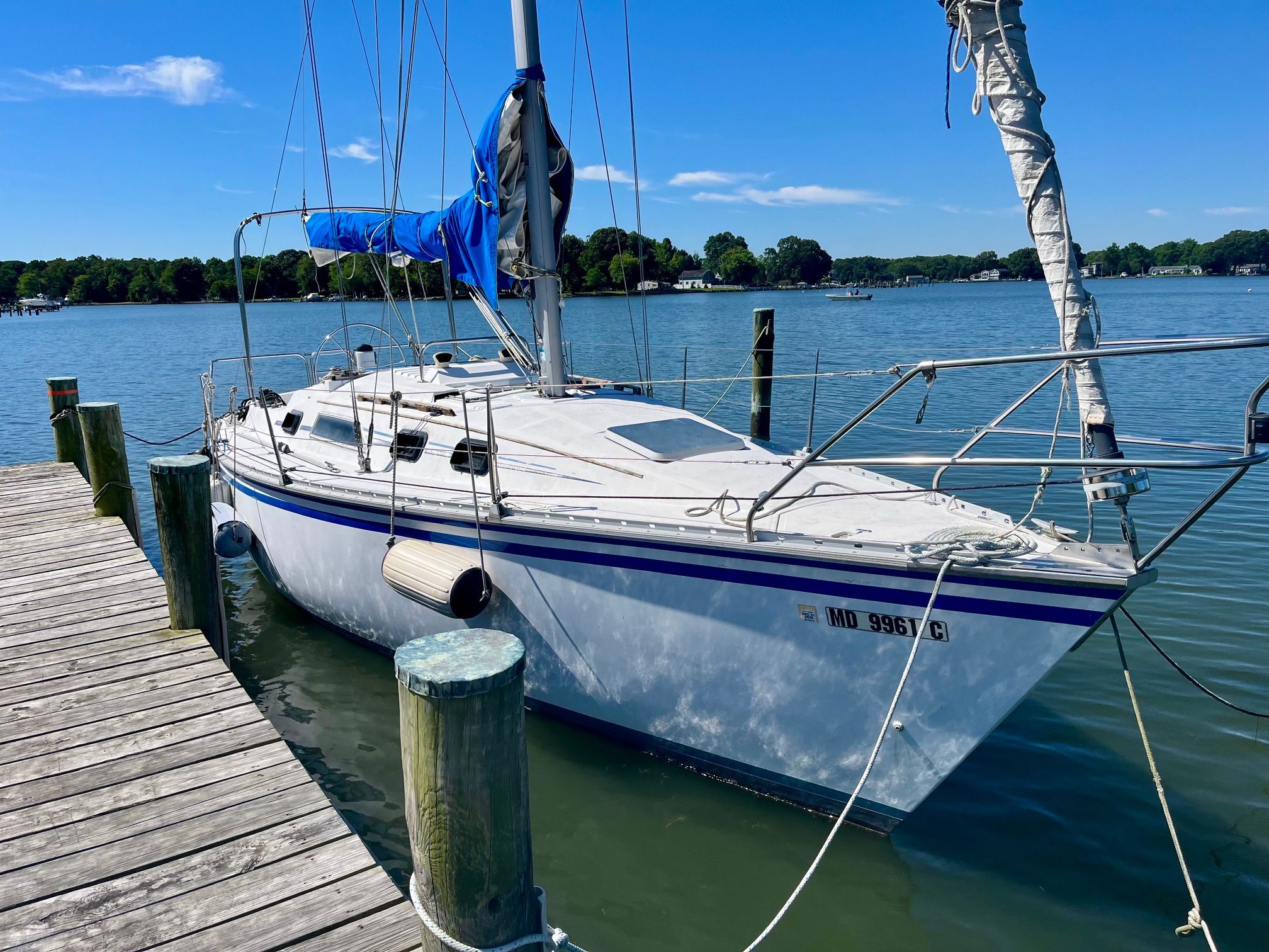A 1985 Hunter 30 sailboat is docked at a wooden pier. It features a blue sail.
