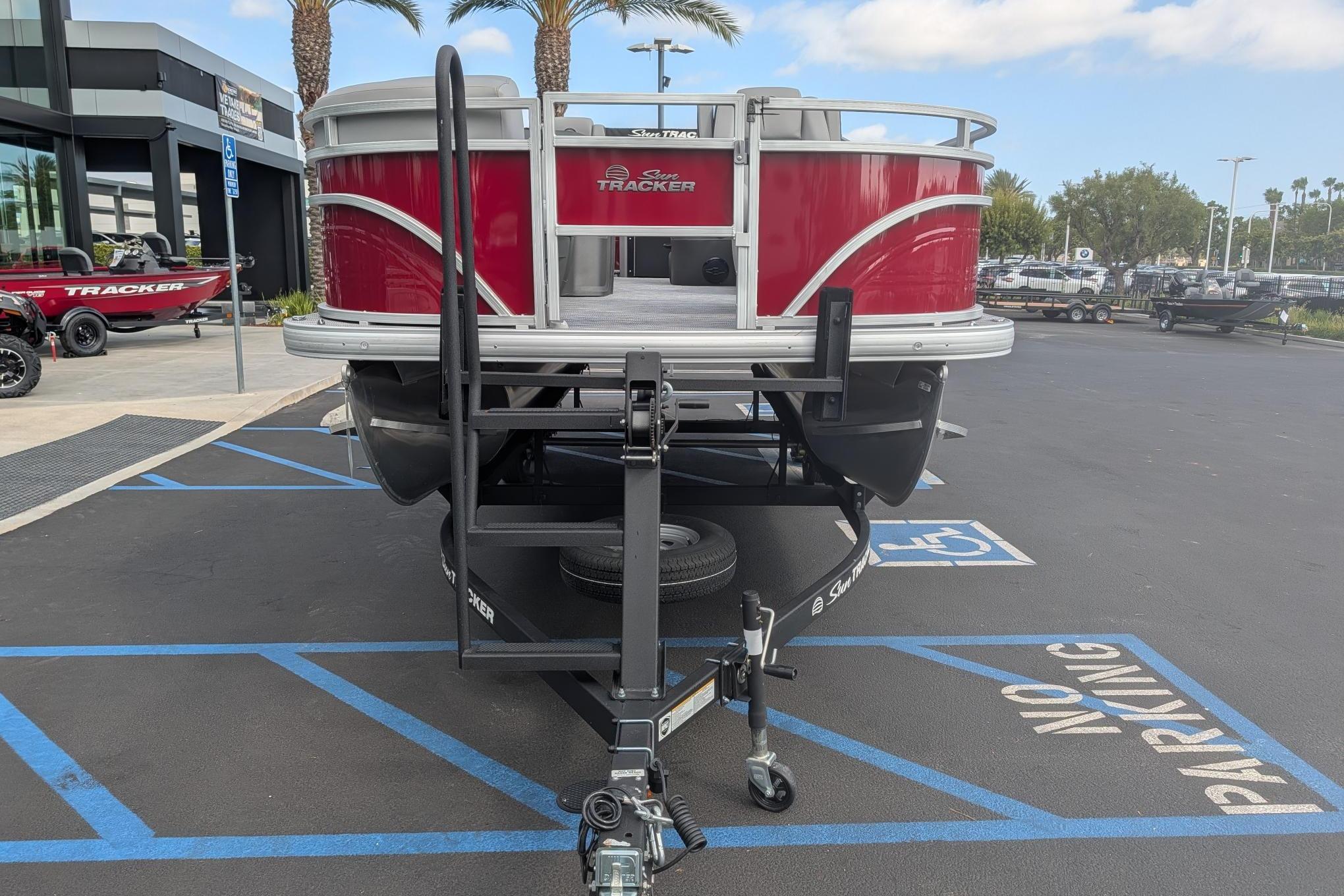 2026 Sun Tracker SportFish 20 DLX pontoon boat on trailer in parking lot.