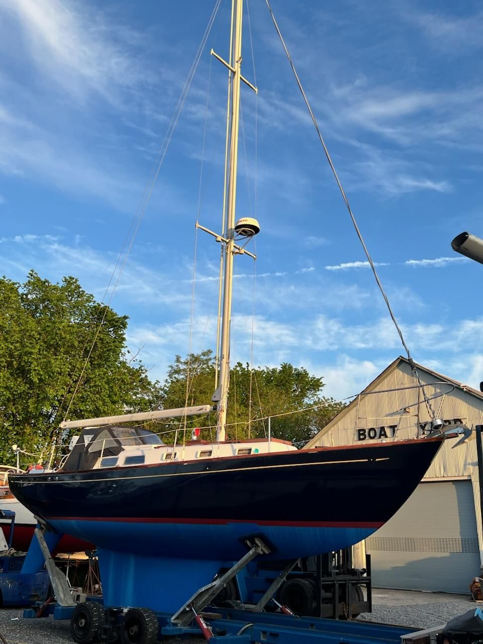1967 Jensen Cal 36 sailboat on trailer, blue sky background, near boatyard.