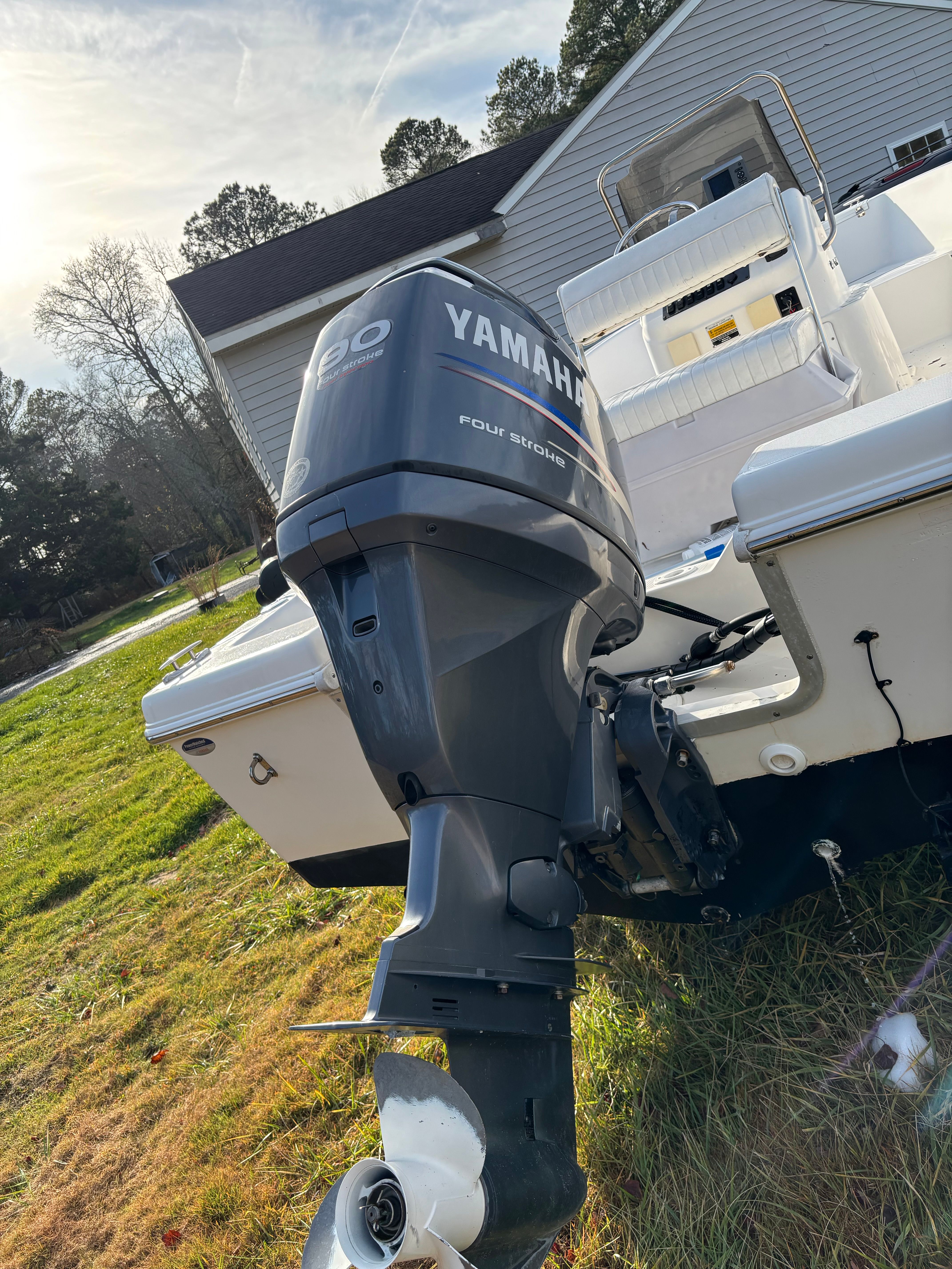 A boat with a Yamaha outboard motor is on grass in front of a house.