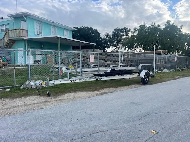 Boat trailer in front of a house with fence and trees.