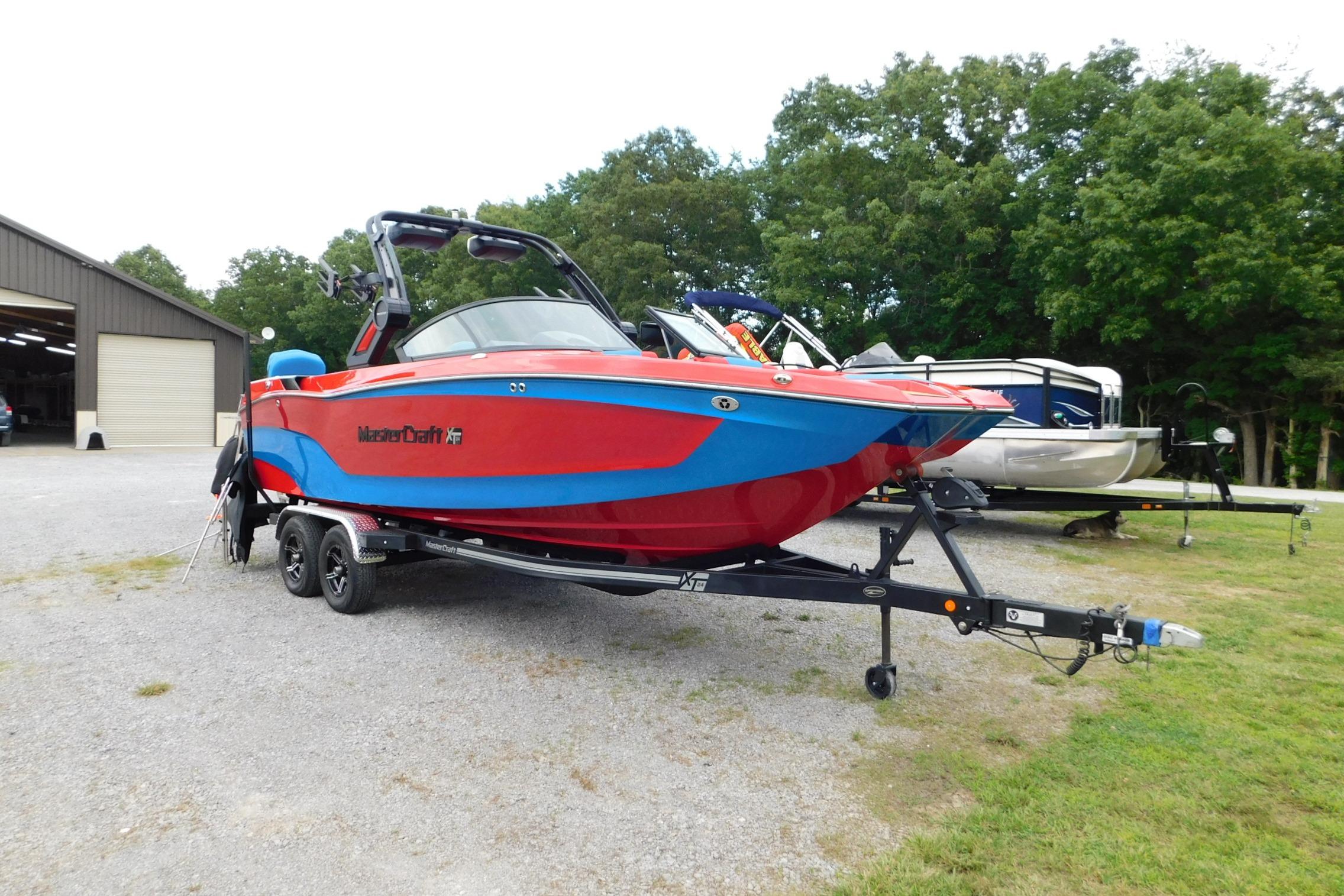 2022 MasterCraft NXT24 boat in vibrant red and blue, parked on a trailer outdoors.