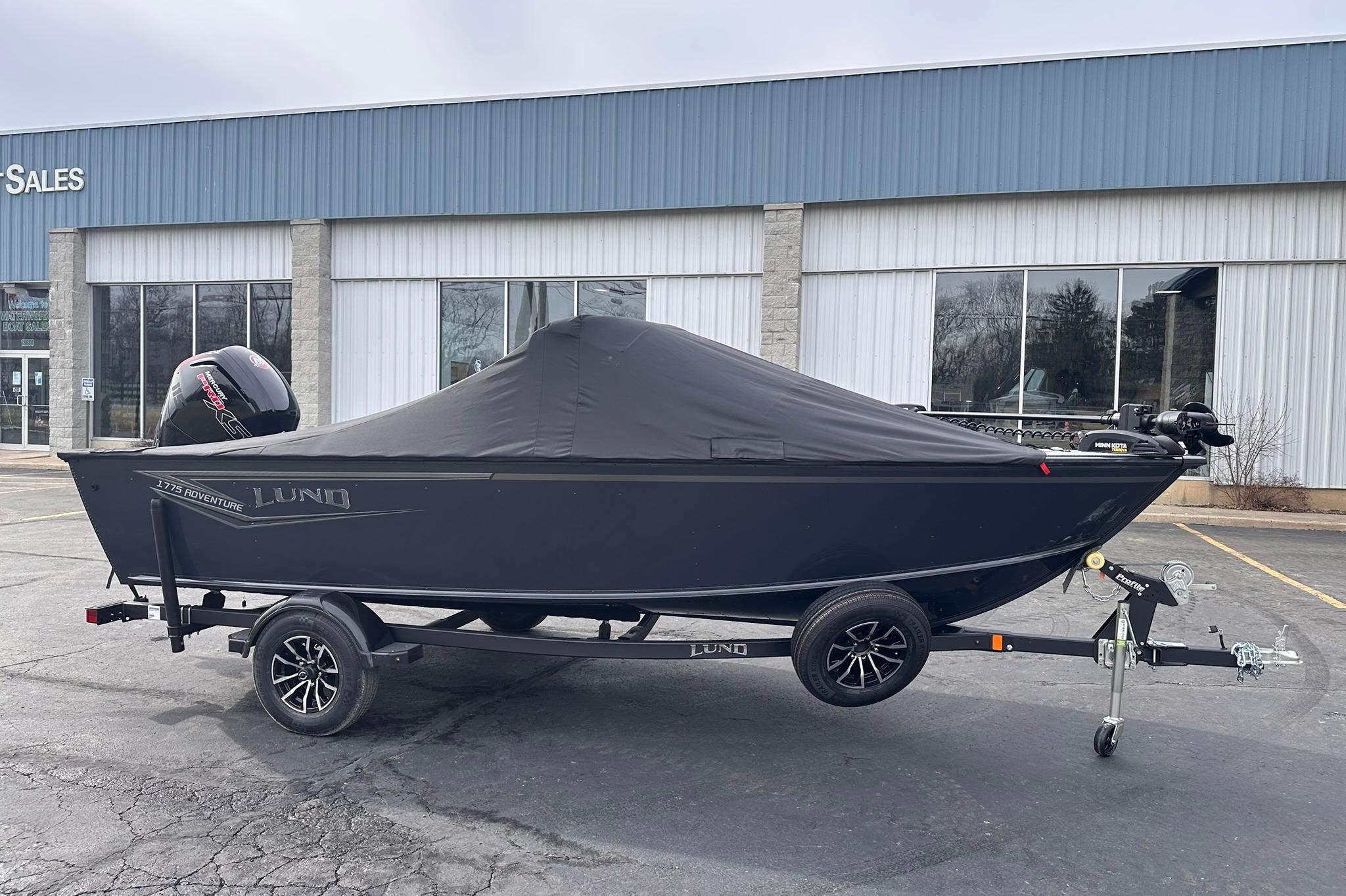 2026 Lund 1775 Adventure Sport boat with cover on trailer, parked outside sales building.