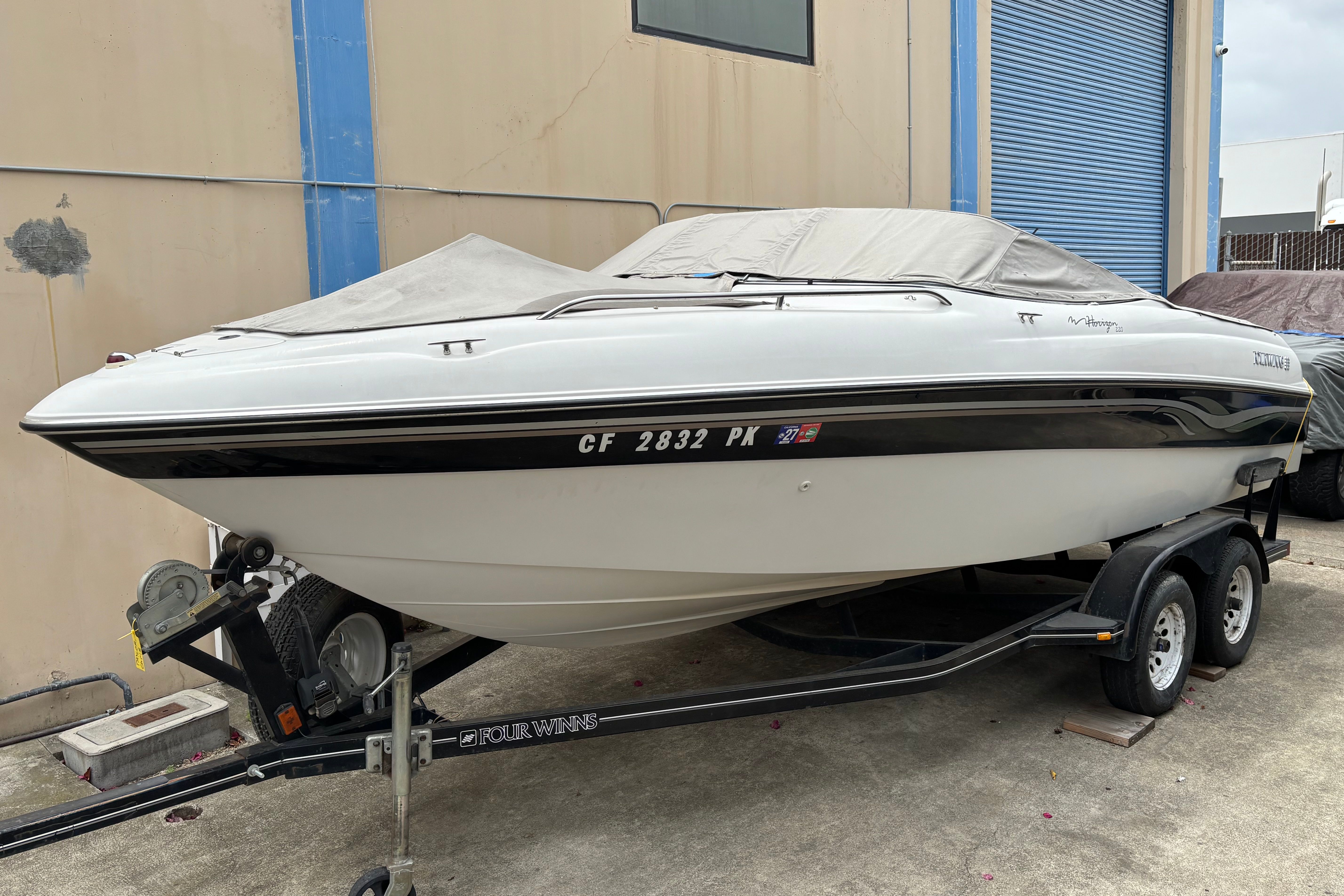 A white motorboat on a trailer, covered with a gray tarp.