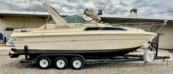 1987 Sea Ray 270 Sundancer boat on a triple-axle trailer, parked outdoors.