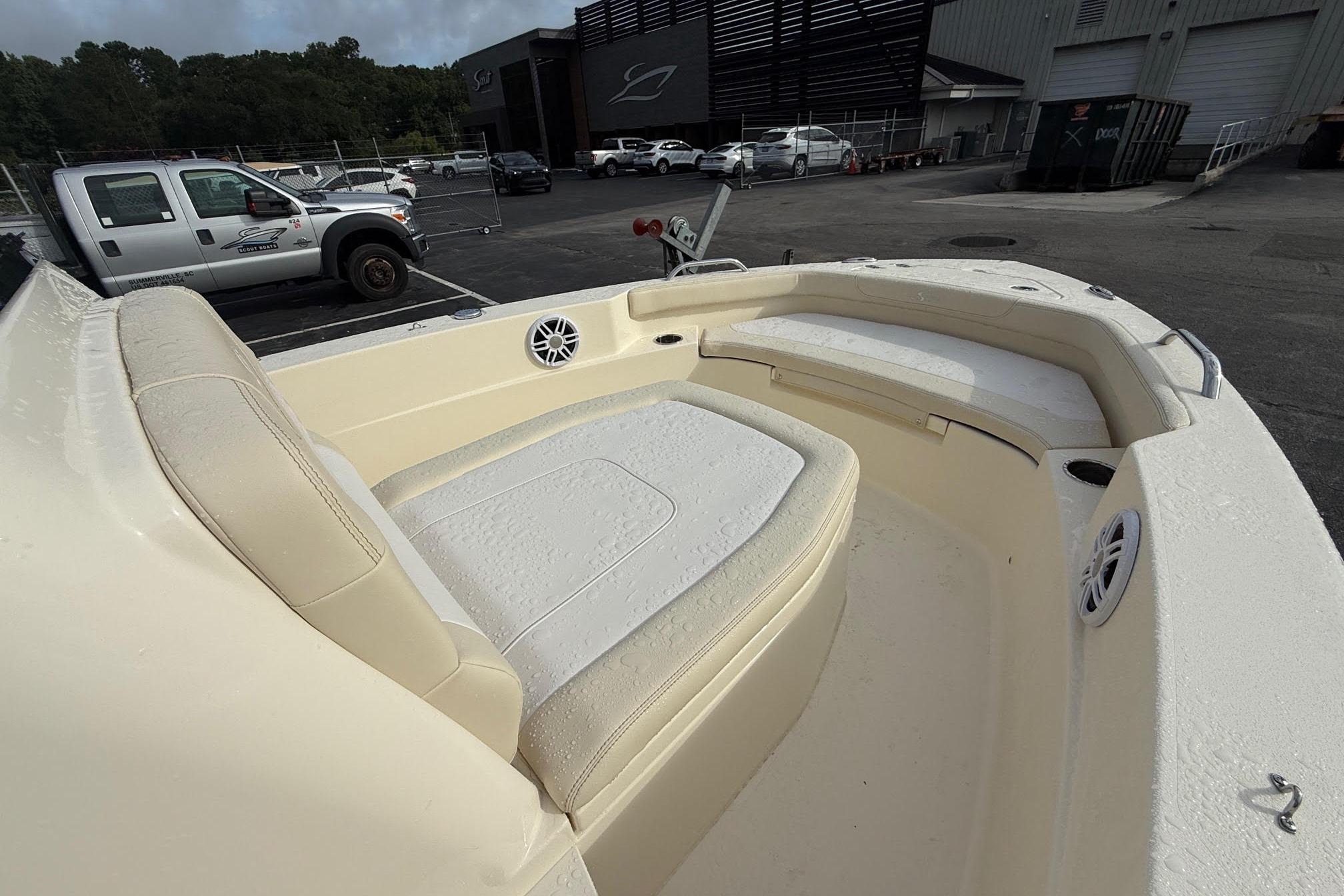 2026 Scout 188 Sportfish boat interior with beige seating and speakers, parked outdoors.