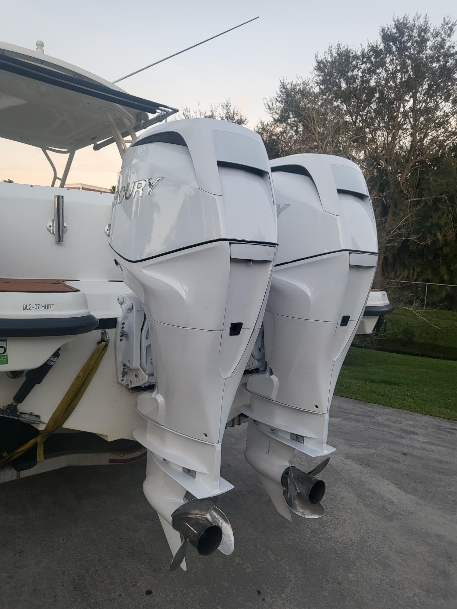 Two white outboard motors on a boat, parked on a trailer, with trees in the background.