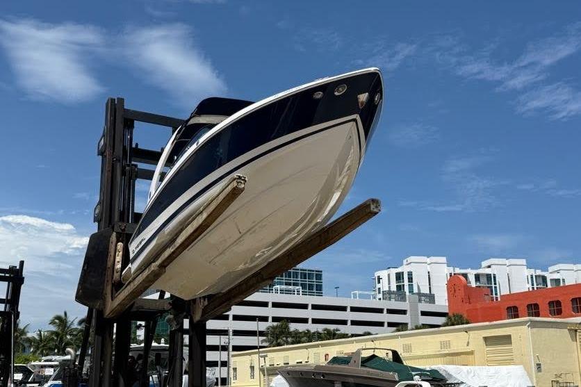 2014 Regal 2500 Bowrider boat lifted by forklift against blue sky.