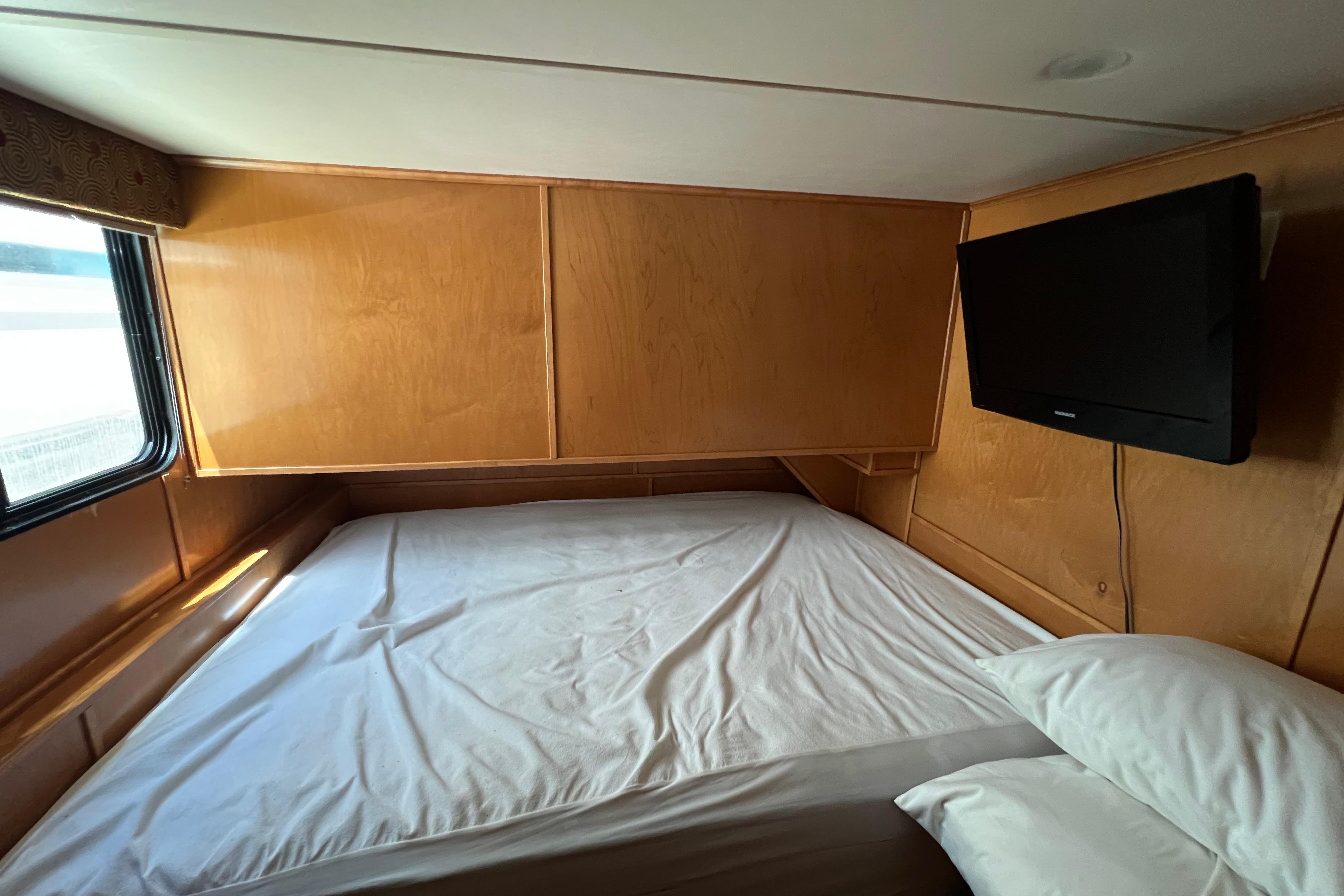 Cozy bedroom in 2013 Destination Yacht Lotta Yachta with wood paneling and mounted TV.
