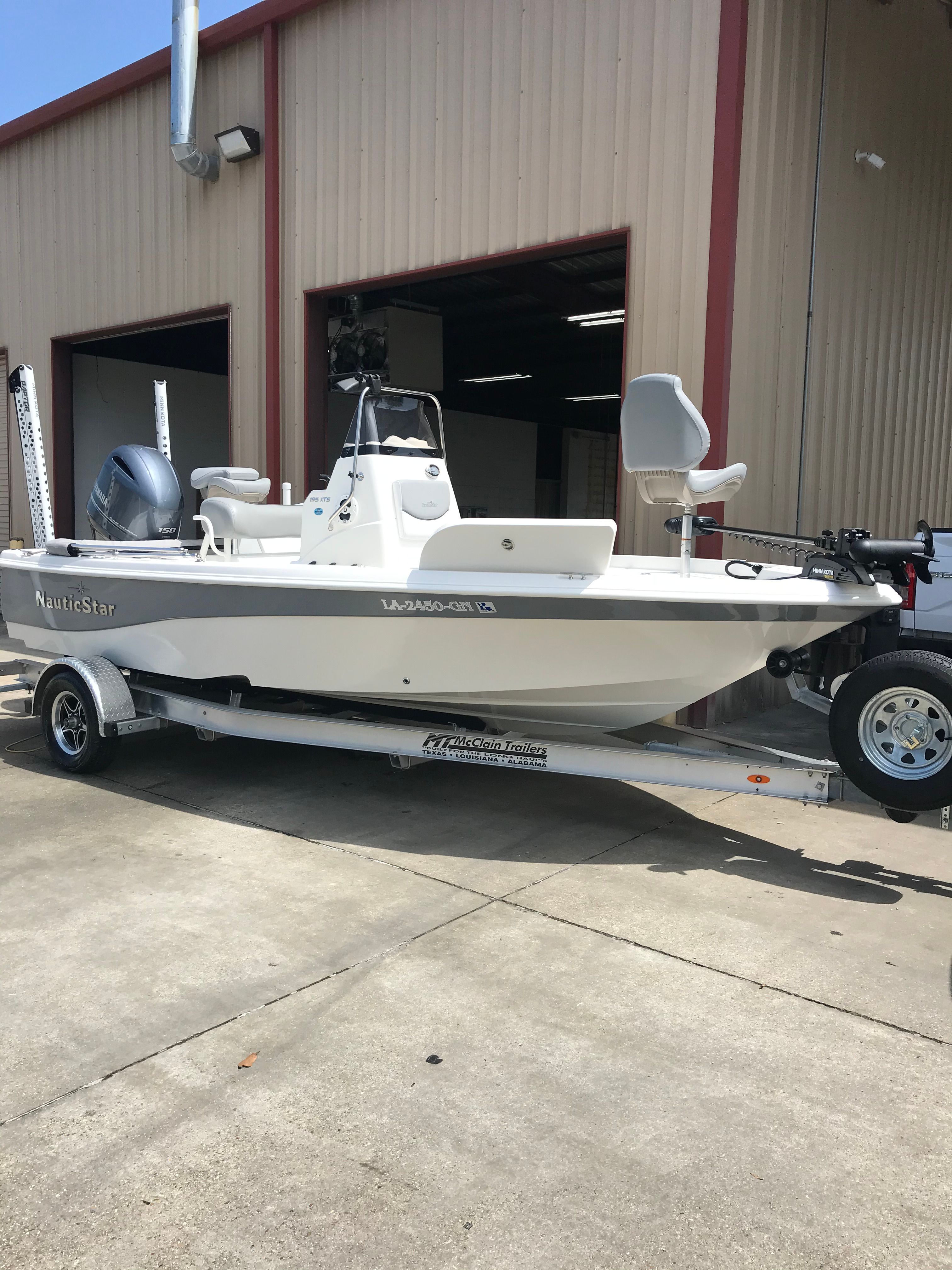A white 2021 NauticStar 195 XTS boat on a trailer outside a warehouse.